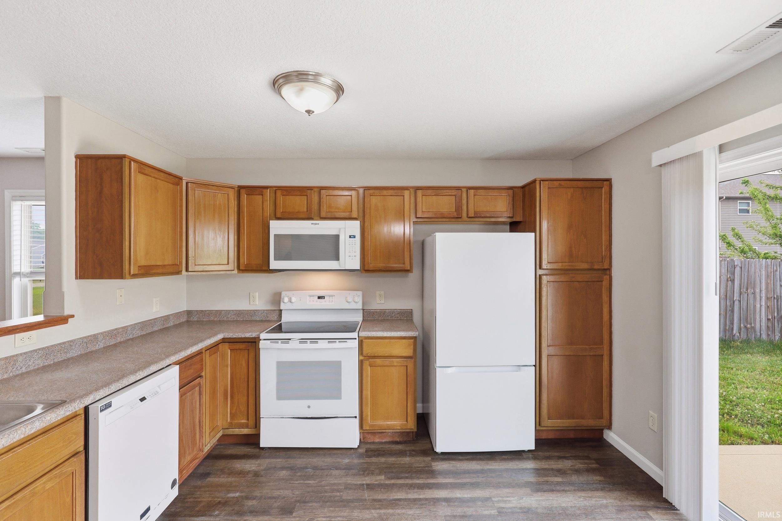 Kitchen featuring wood-finish cabinetry, white appliances, and a sliding glass door providing access to the backyard