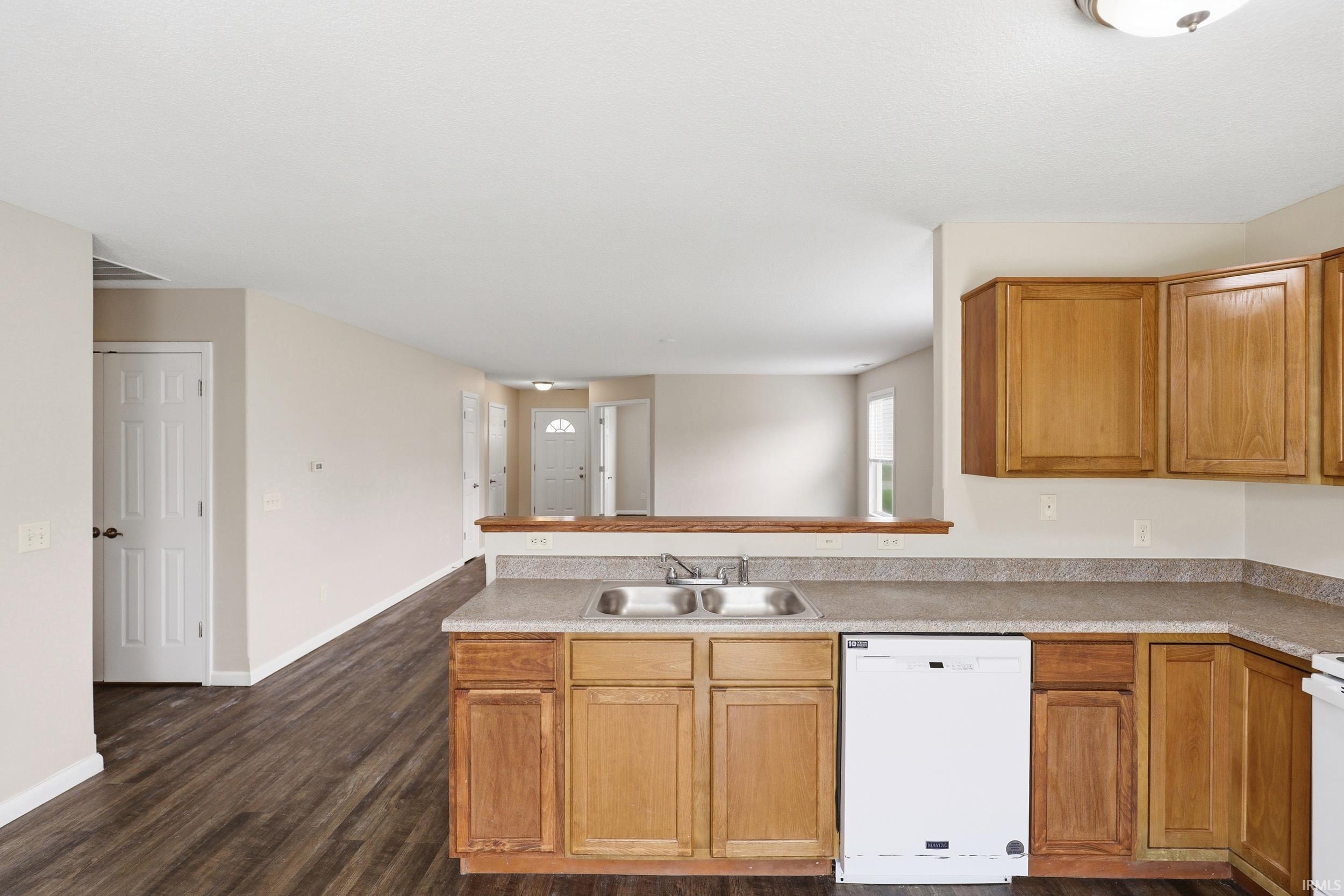 Kitchen featuring wood cabinetry, stainless steel double basin sink, and a white dishwasher