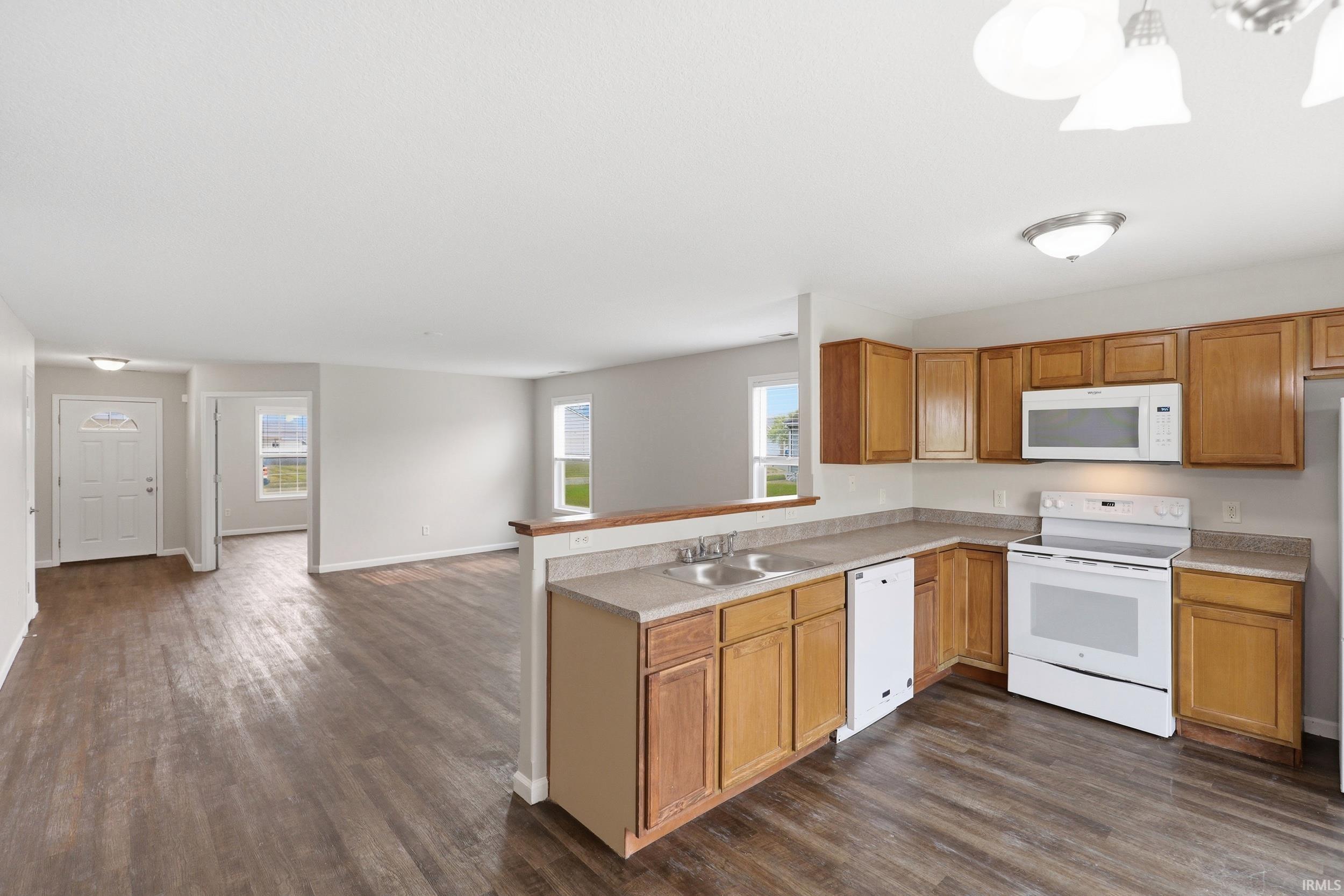 Open-concept kitchen with wood-finish flooring, light wood cabinetry, white appliances, and a double basin sink