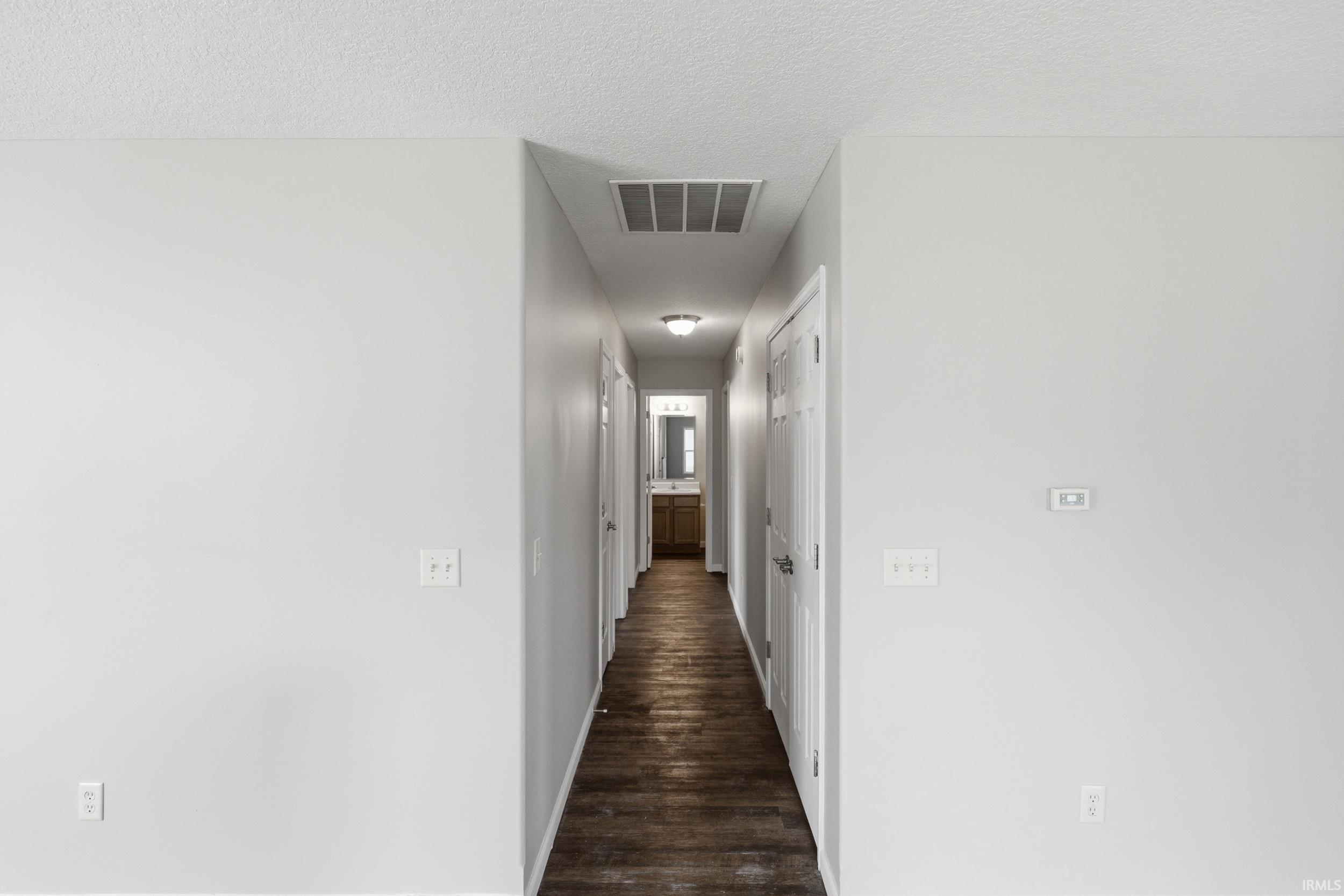 Long hallway featuring wood-finish flooring, light grey walls, and a visible bathroom with a wood-finish vanity at the far end
