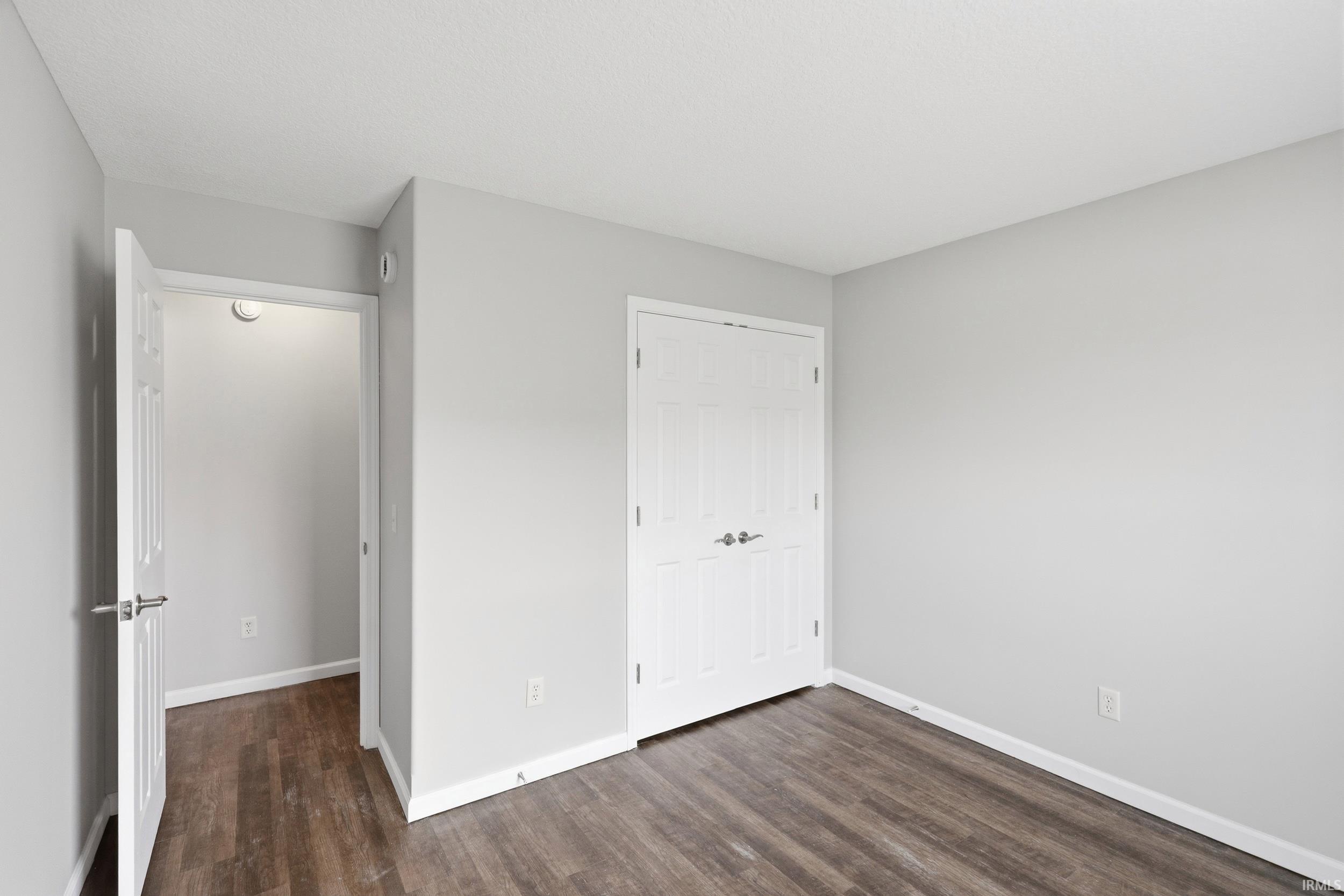 Room featuring wood-finish flooring, light grey walls, white trim, and a white six-panel bifold closet door