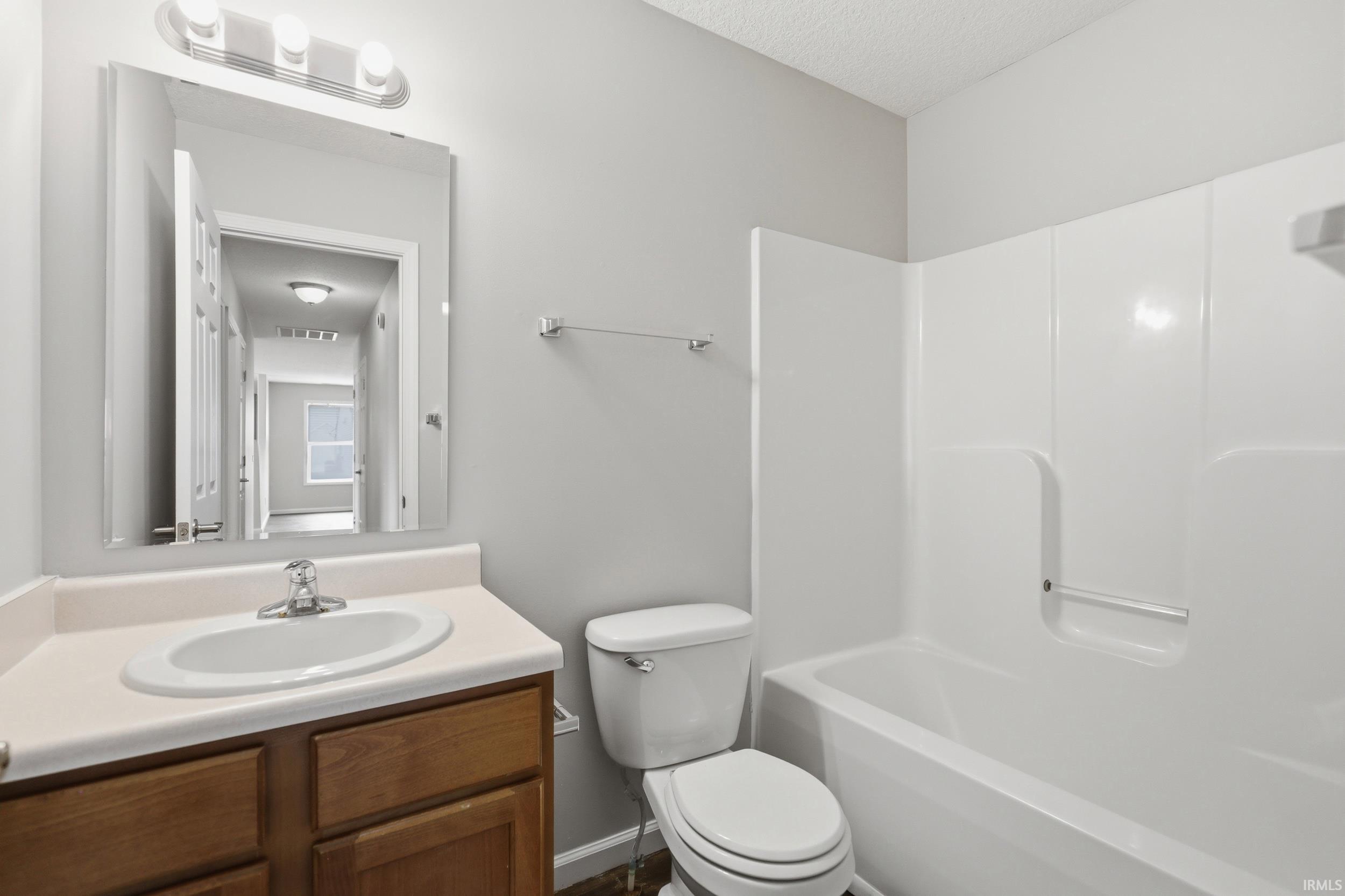 Bathroom featuring a white bathtub, white toilet, and wood-finish vanity with a white countertop and integrated sink