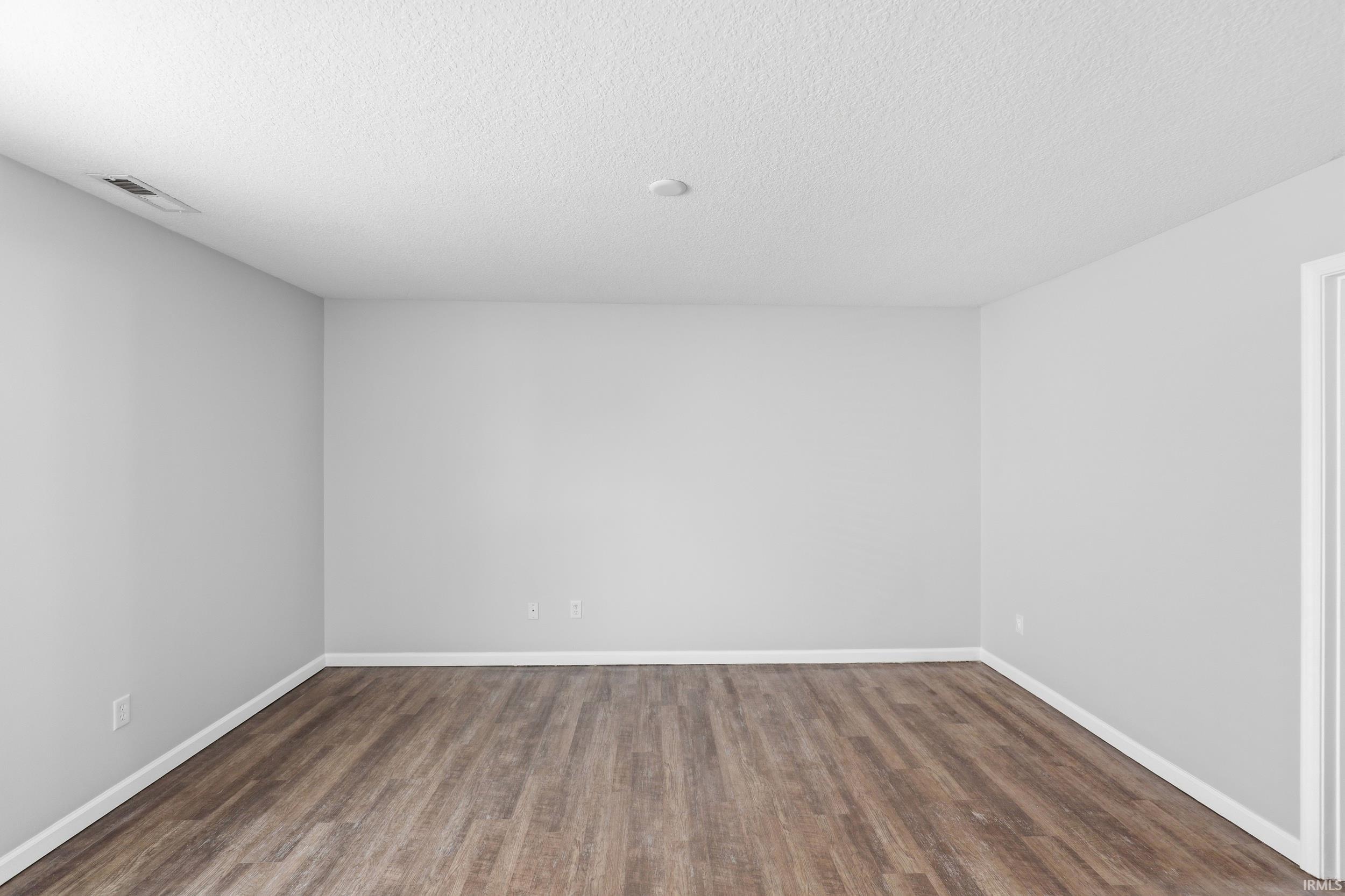 Spacious room featuring wood-finish flooring, light grey walls, and white baseboards
