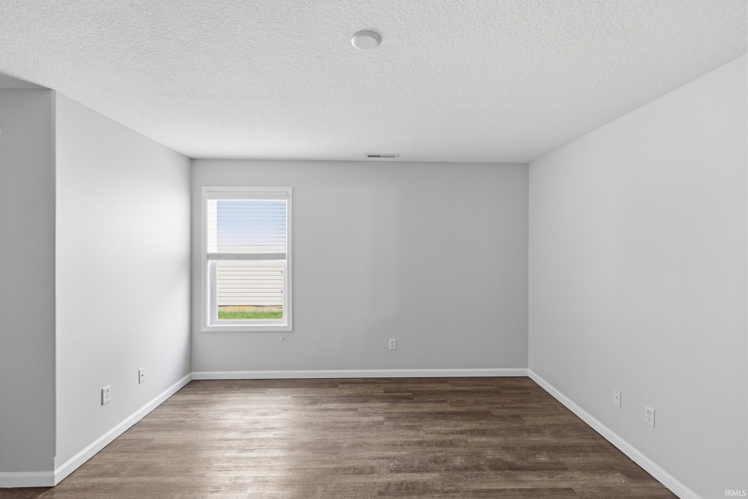 Spacious room featuring wood-finish flooring, light grey walls, white baseboards, and a single window with blinds