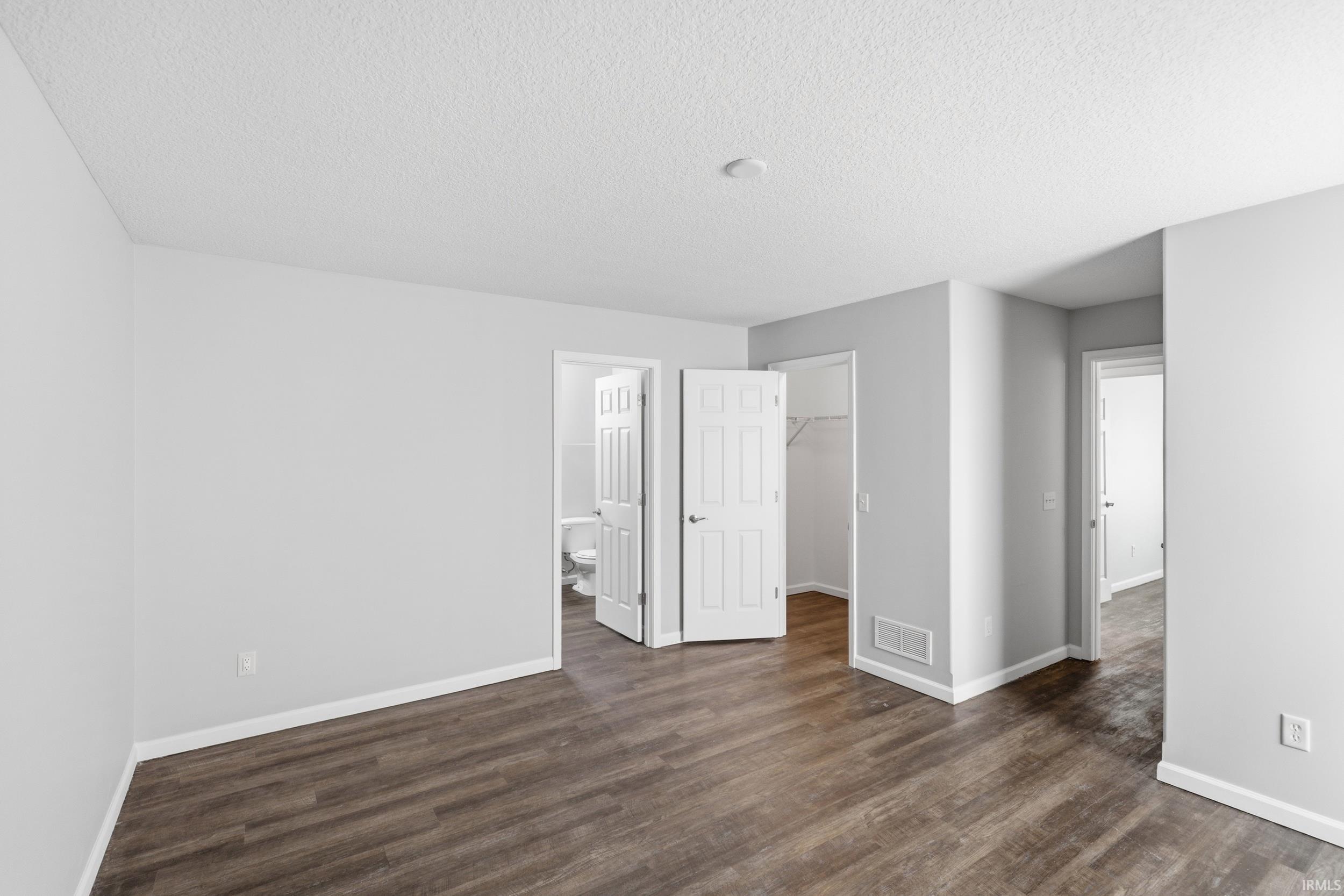 Spacious room featuring wood-finish flooring, light grey walls, white baseboards, and white paneled doors