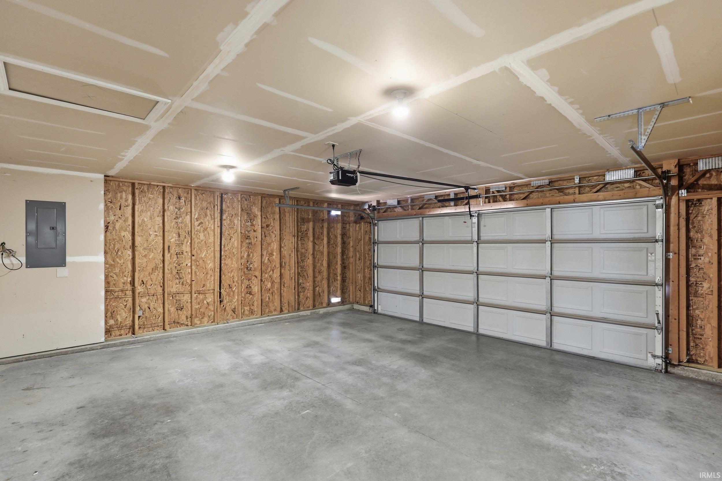 Spacious two-car garage featuring a concrete floor, exposed wood framing, and a white paneled garage door with an automatic opener