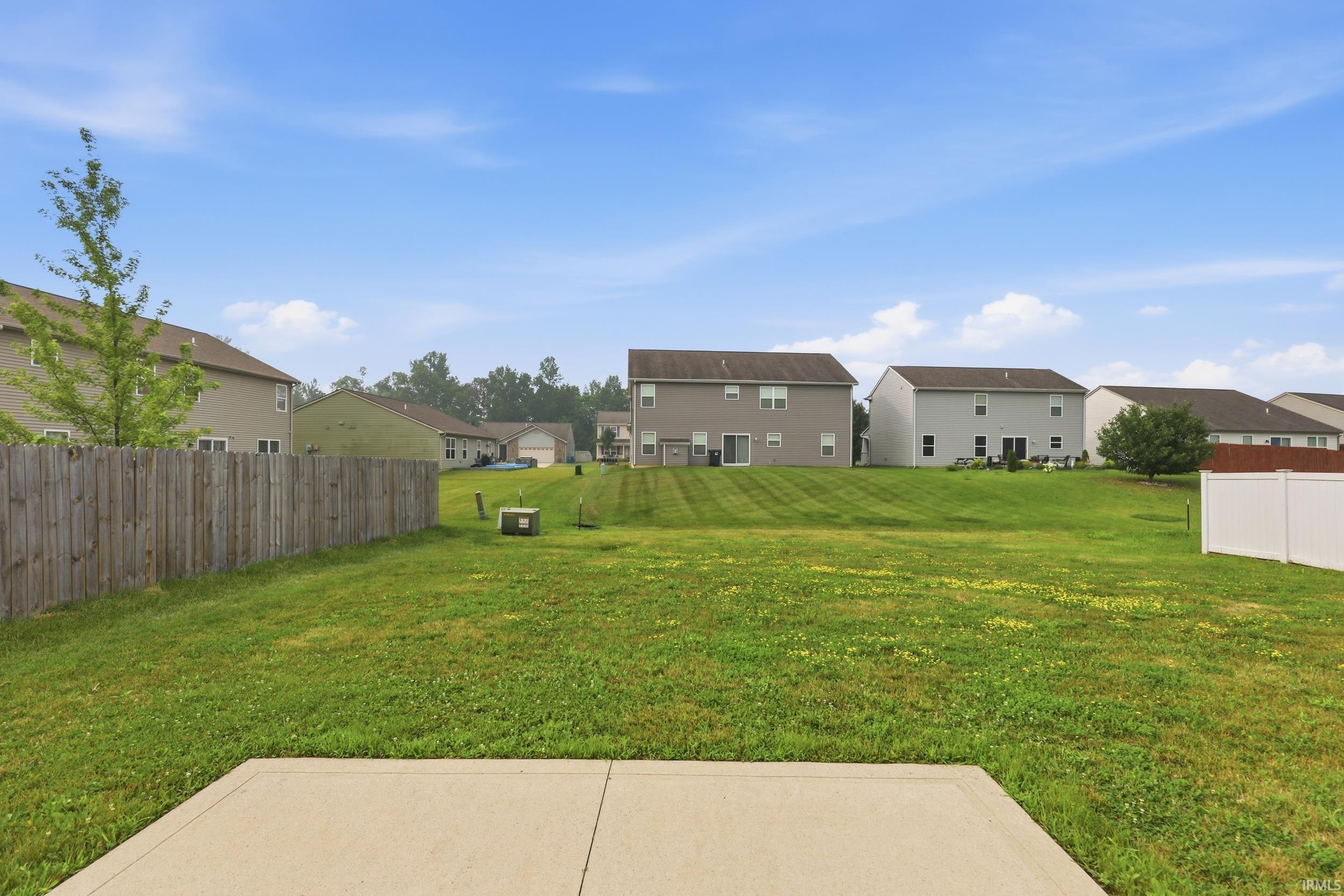 Expansive green space featuring a concrete patio, wood privacy fencing, and a separate white vinyl fence section