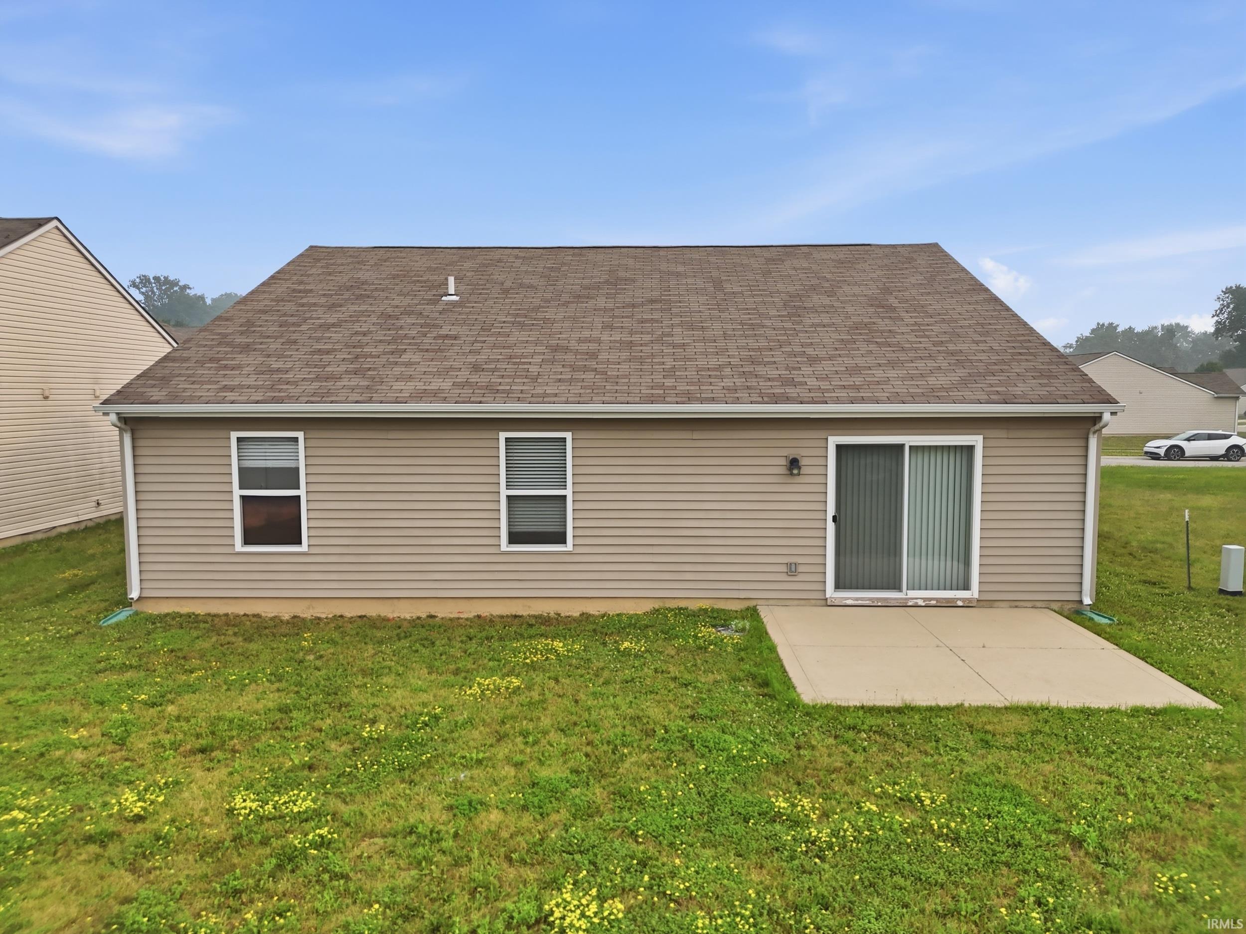 Rear exterior featuring tan horizontal siding, a sliding glass door, a concrete patio, and a shingle roof