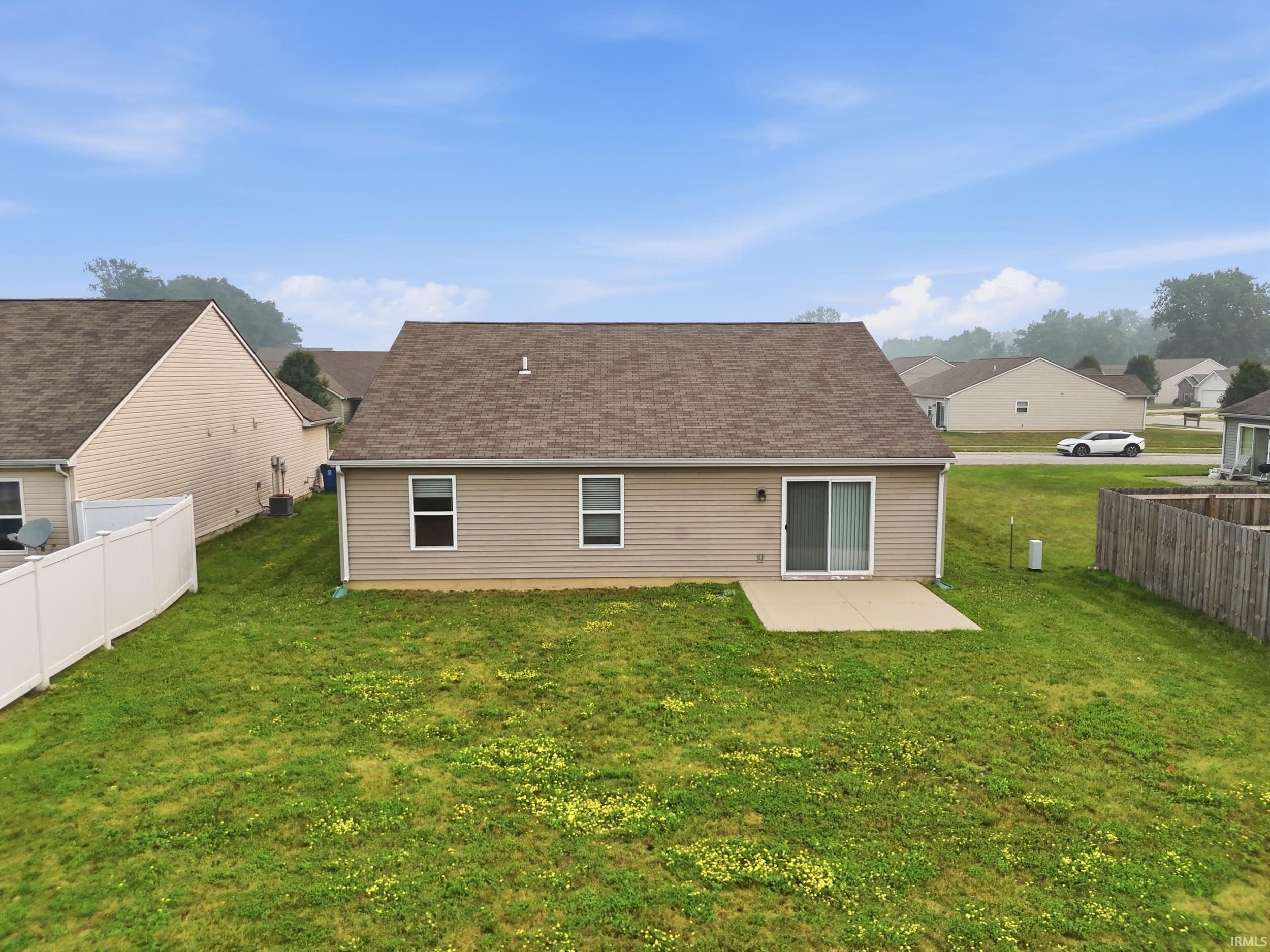 Rear exterior featuring tan siding, a brown shingle roof, and a concrete patio