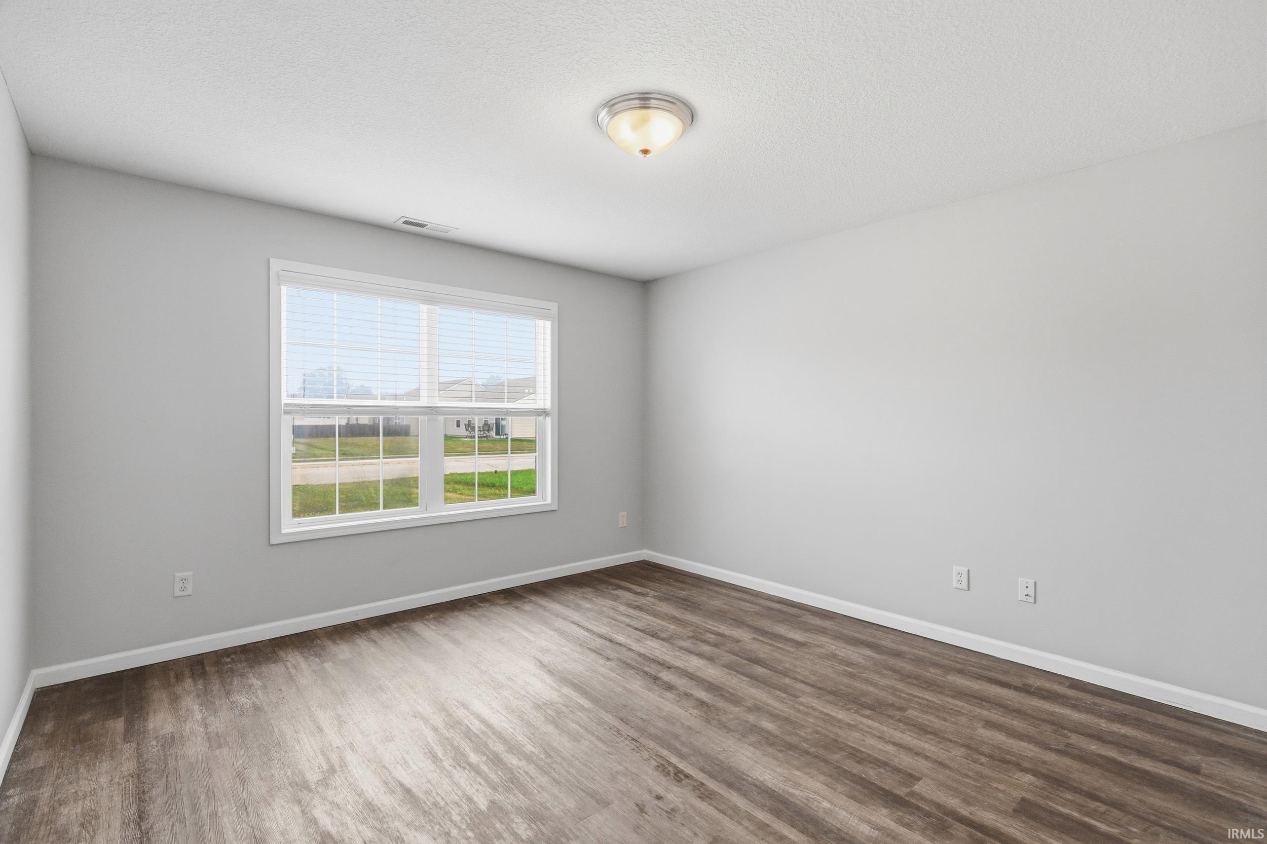 Spacious room featuring wood-finish flooring, light gray walls, a window with white blinds, and a ceiling-mounted light fixture