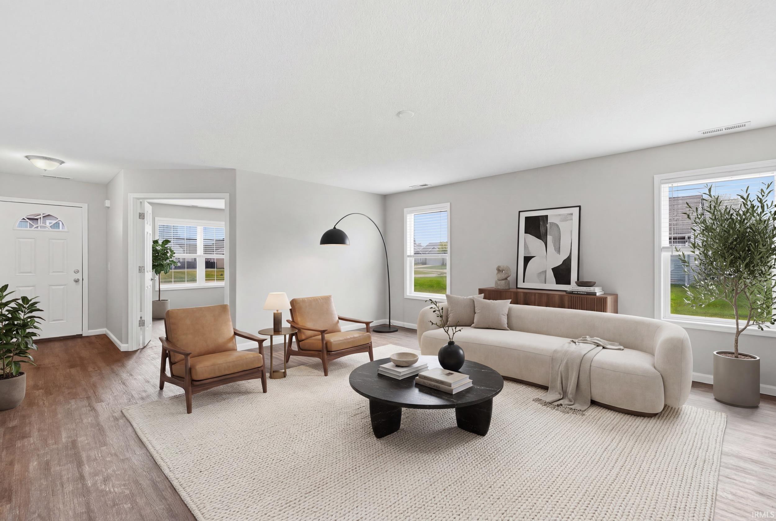 Spacious living area featuring wood-finish flooring, light wall tones, and multiple windows