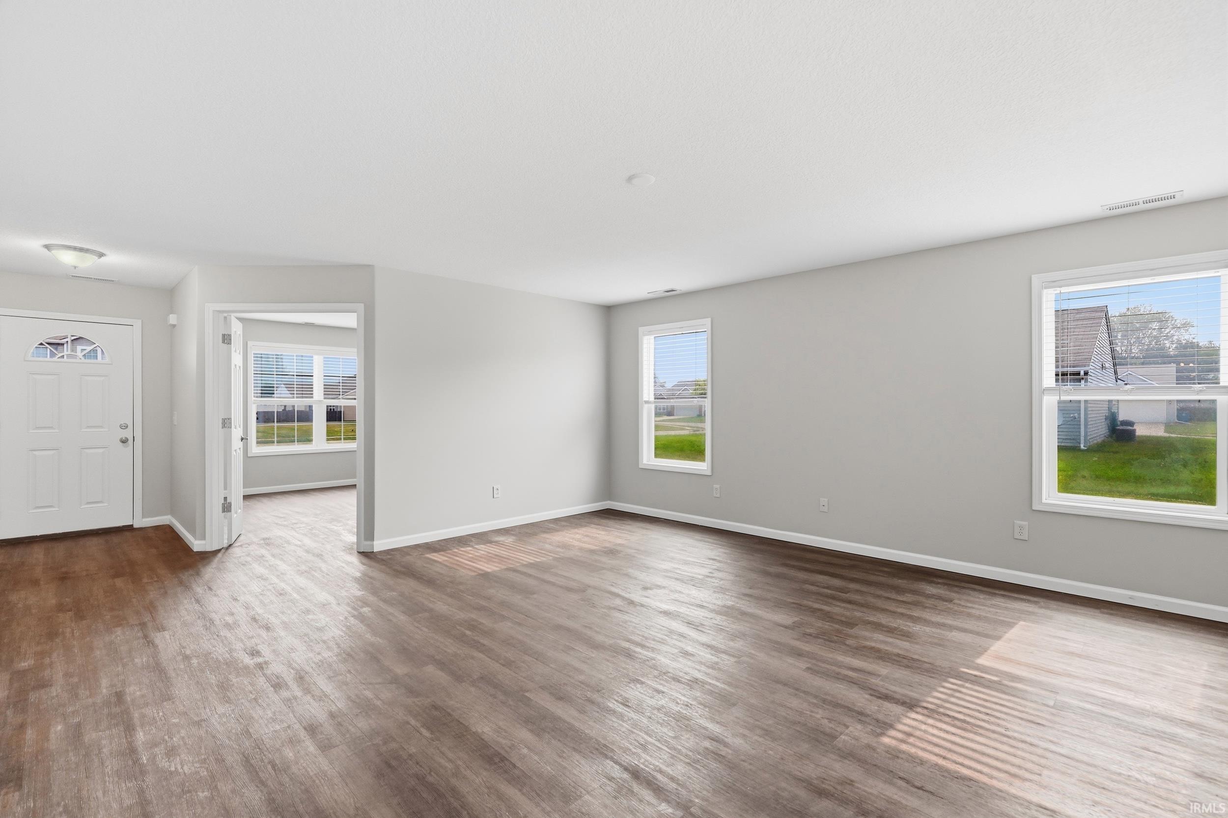 Spacious interior featuring wood-finish flooring, light grey painted walls, white trim, and multiple windows