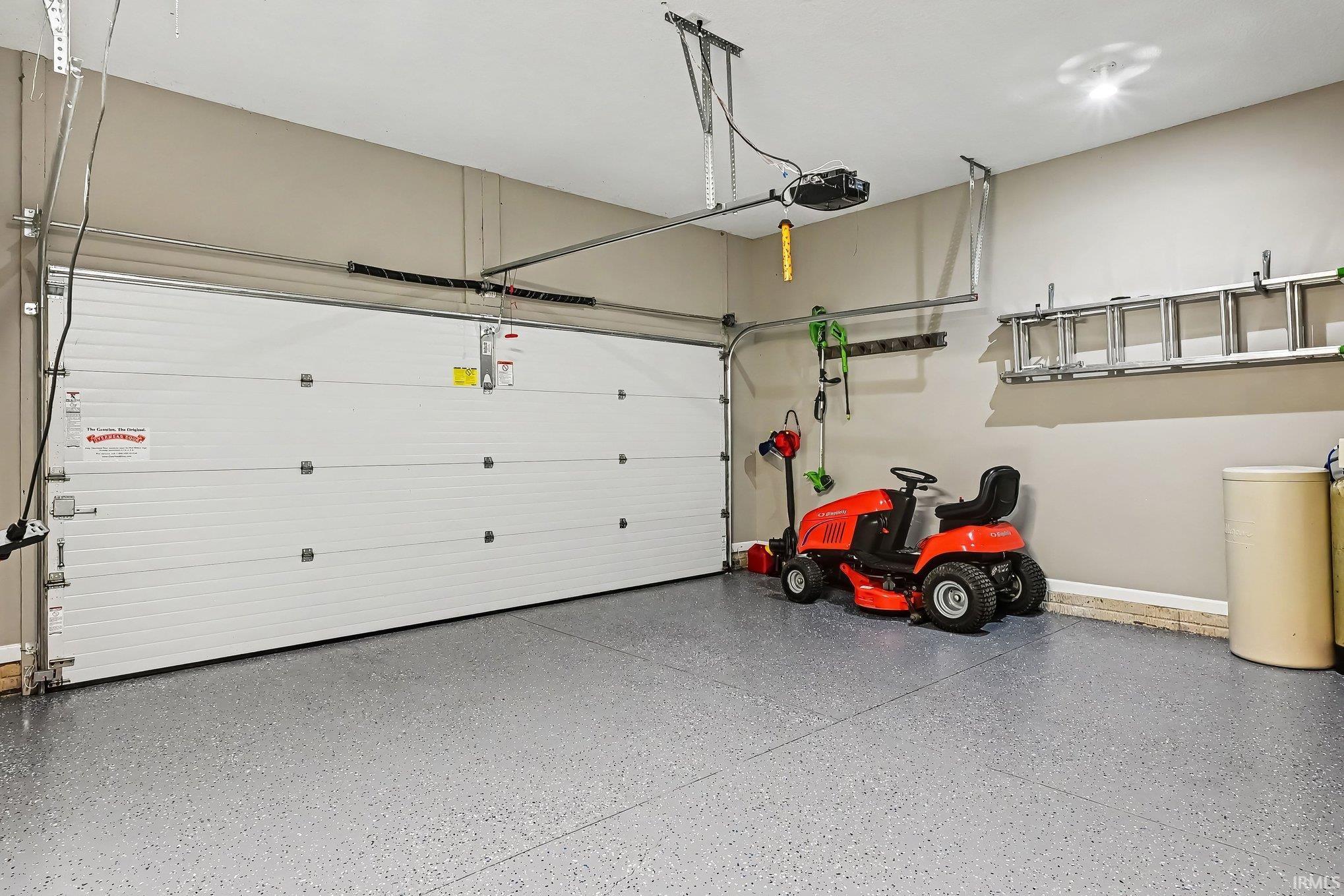 Garage featuring a sectional overhead door with automatic opener, gray epoxy flooring, painted walls, and overhead lighting