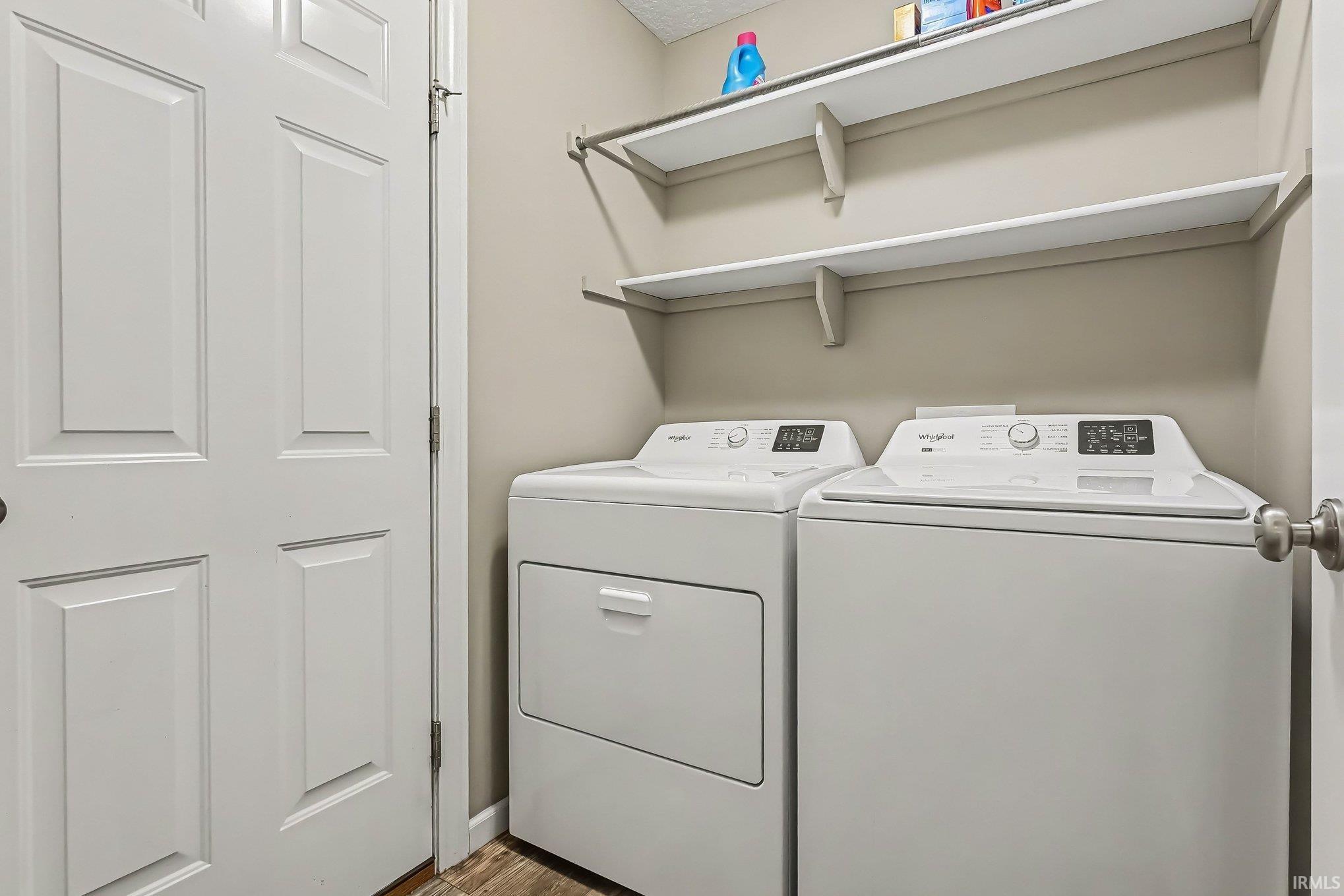 Dedicated laundry area featuring a white washer and dryer pair, two wall-mounted storage shelves, and wood-finish flooring