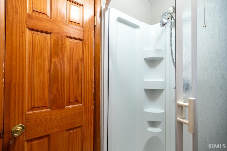 Compact shower enclosure with integrated shelving and a textured glass door, complemented by a paneled wood door with a brass-finish doorknob