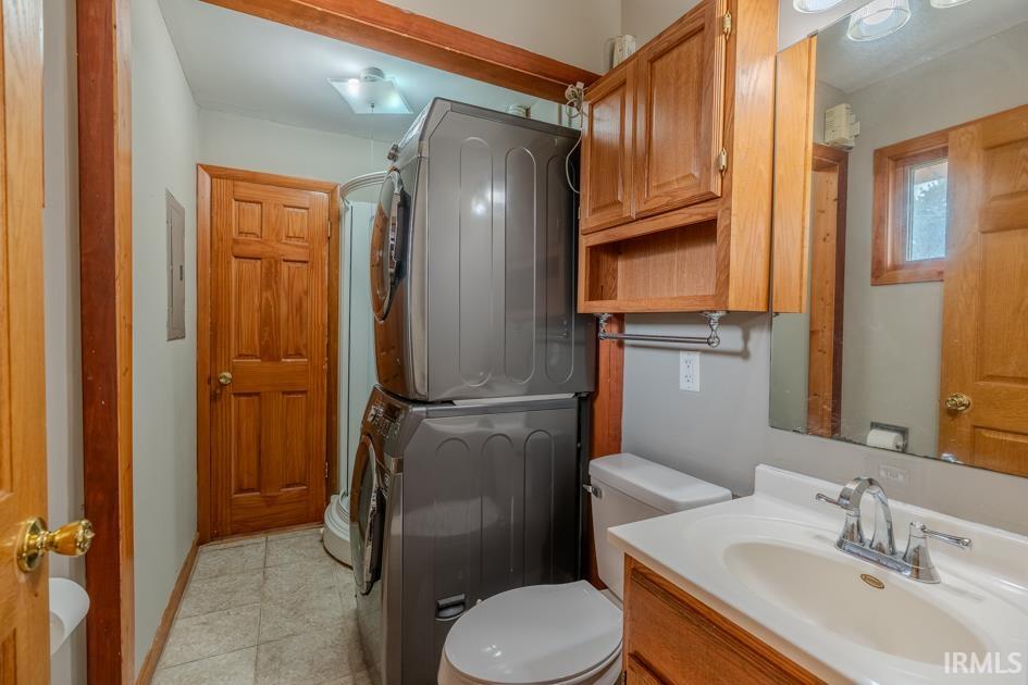 Bathroom featuring tile flooring, a shower stall, wood vanity with integrated sink, wood-finish cabinetry, and a stacked laundry unit