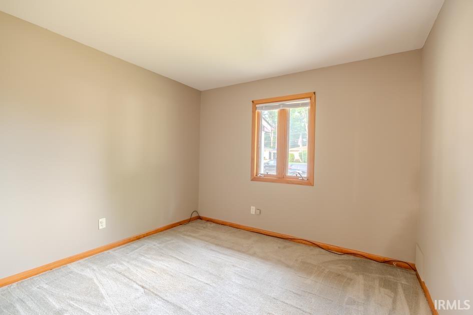Neutral-toned interior with light tan walls, a single window featuring wood trim, and light-colored carpeting
