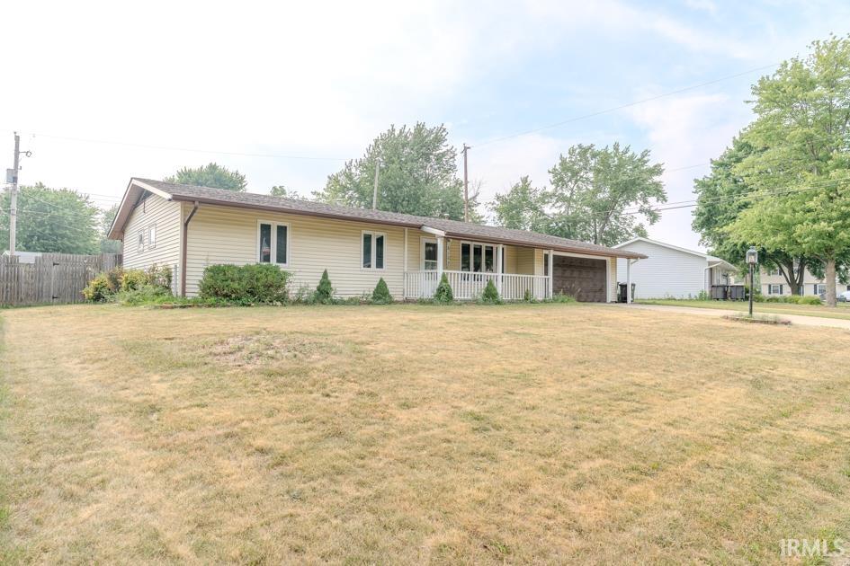 Ranch-style residence featuring light-colored siding, a covered front porch with white railings, an attached garage, and established landscaping