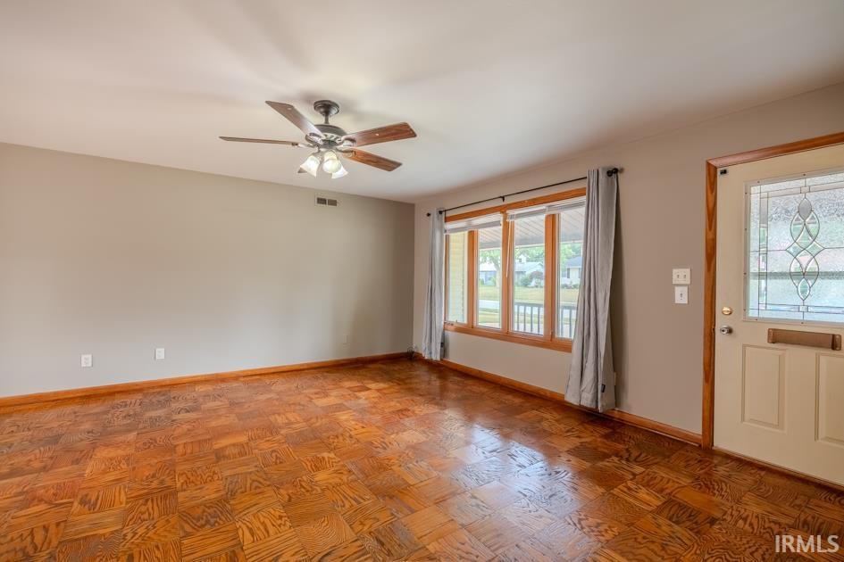 Living area featuring wood-finish flooring, a multi-pane window with wood trim, and a ceiling fan with light fixture