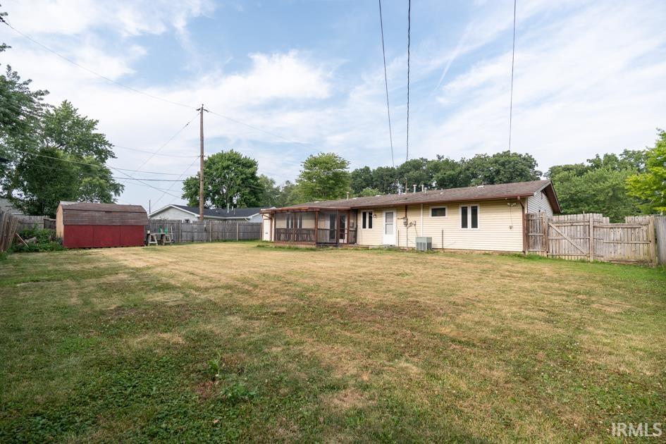 Expansive fenced backyard featuring a wood fence, detached storage shed, covered porch, and light-colored siding