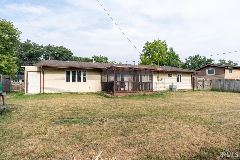 Expansive backyard featuring a screened-in porch with wood railing, tan vinyl siding, multiple windows, and a wood privacy fence