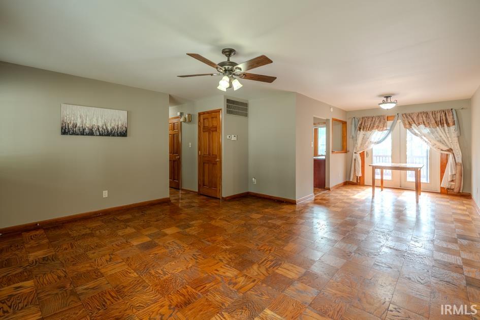 Spacious room with parquet wood flooring, ceiling fan with light fixture, and French doors