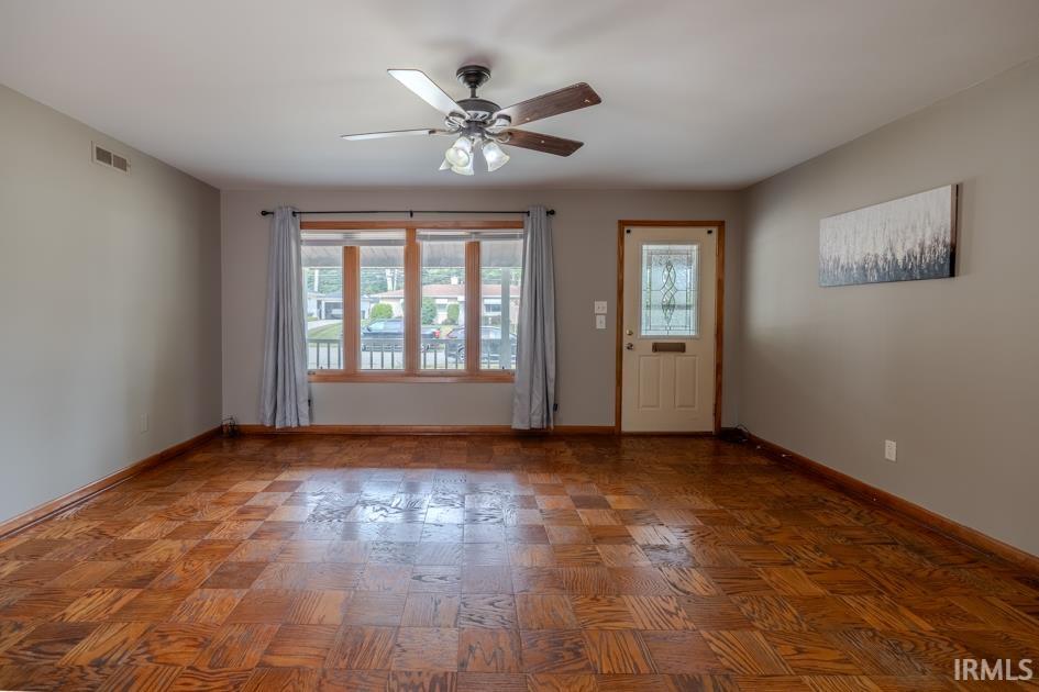 Spacious living area featuring wood-finish flooring, a multi-pane window with wood trim, and a ceiling fan with integrated lighting