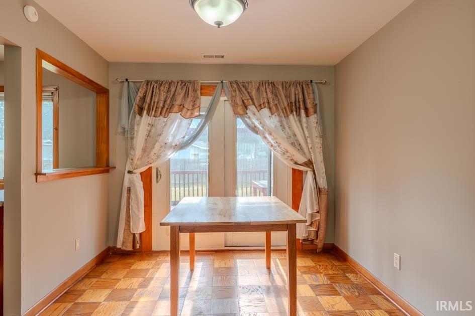Light-filled room featuring wood-finish parquet flooring, a wood-trimmed pass-through opening, and a glass-paneled patio door leading to an outdoor deck