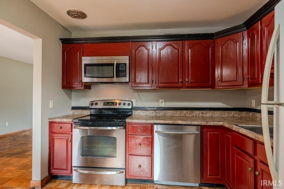 Kitchen featuring red cabinetry with black trim, stainless steel appliances including a microwave, range, and dishwasher, and a light-toned countertop