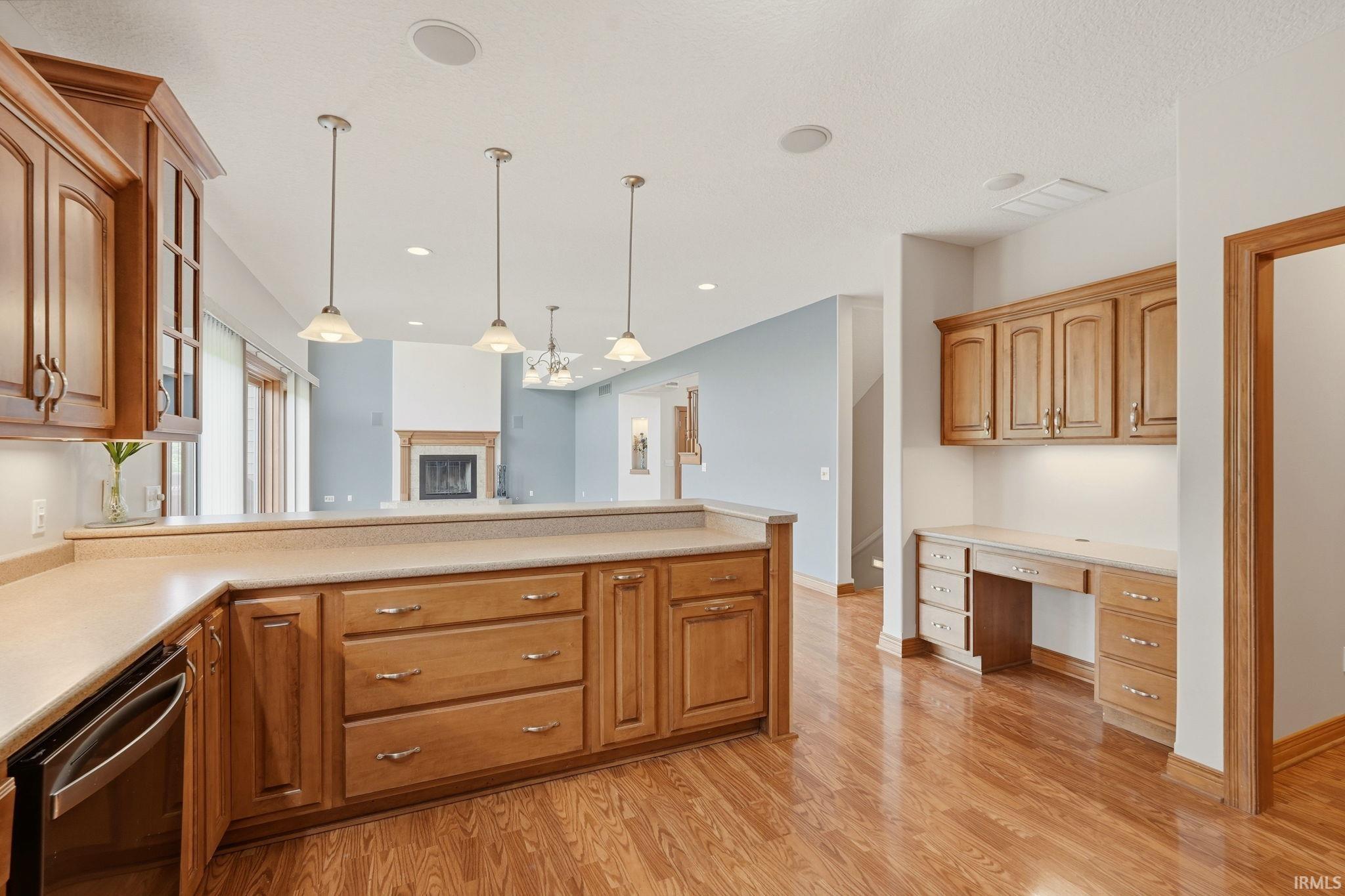 Open-concept living space with wood-finish flooring, a kitchen island featuring integrated cabinetry, recessed lighting, and pendant light fixtures