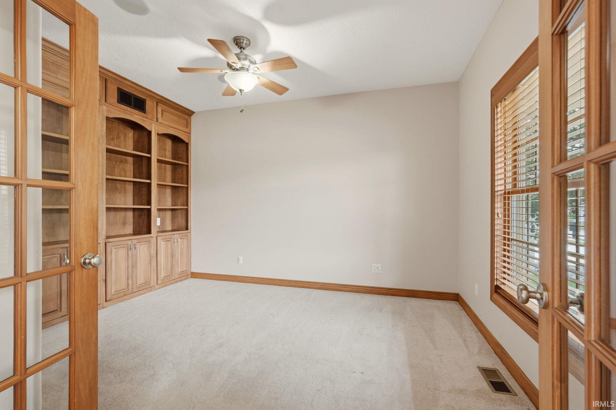 Room featuring built-in wood cabinetry with shelving, carpet flooring, and a ceiling fan with integrated lighting