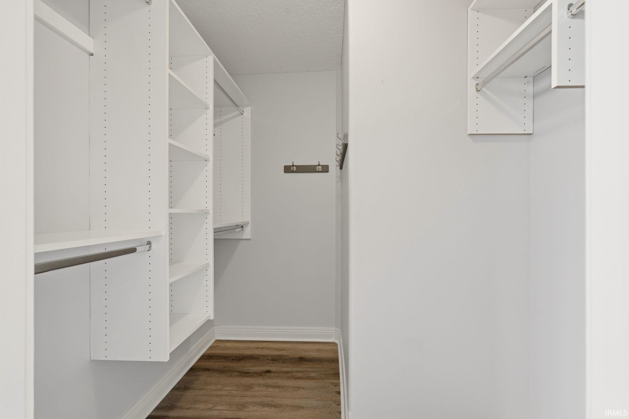 Walk-in closet featuring custom white built-in shelving, multiple hanging rods, and wood-finish flooring