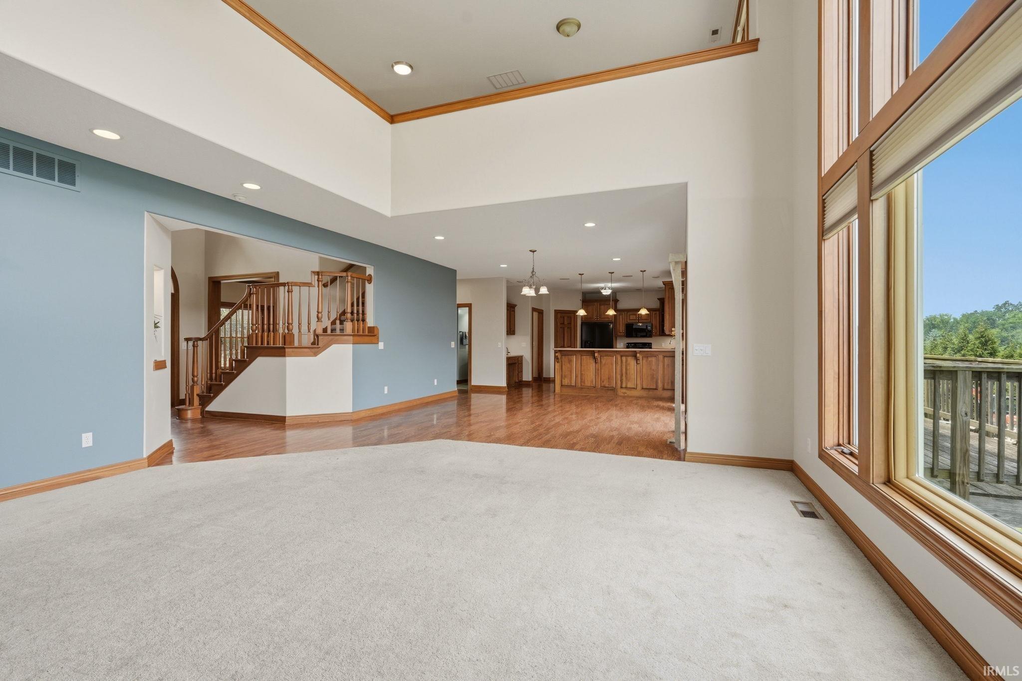 Expansive living space featuring a light-colored carpet, soaring ceilings, and large windows with wood trim