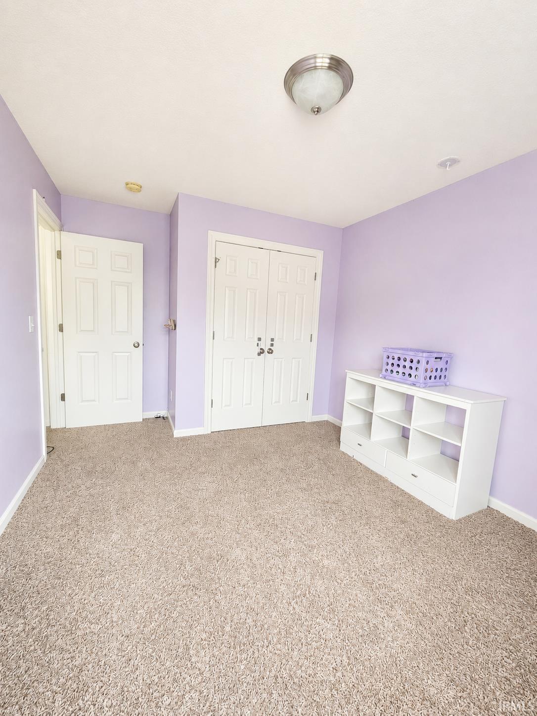 Carpeted room featuring a ceiling-mounted light fixture, two solid core doors with brushed nickel hardware, and an additional closet with bi-fold doors