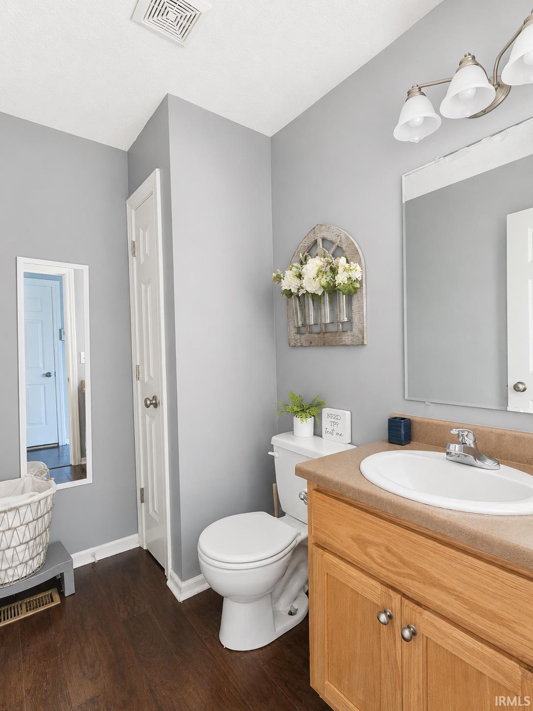 Bathroom featuring wood-finish flooring, a light wood vanity with a beige countertop, an undermount sink, and a three-light fixture