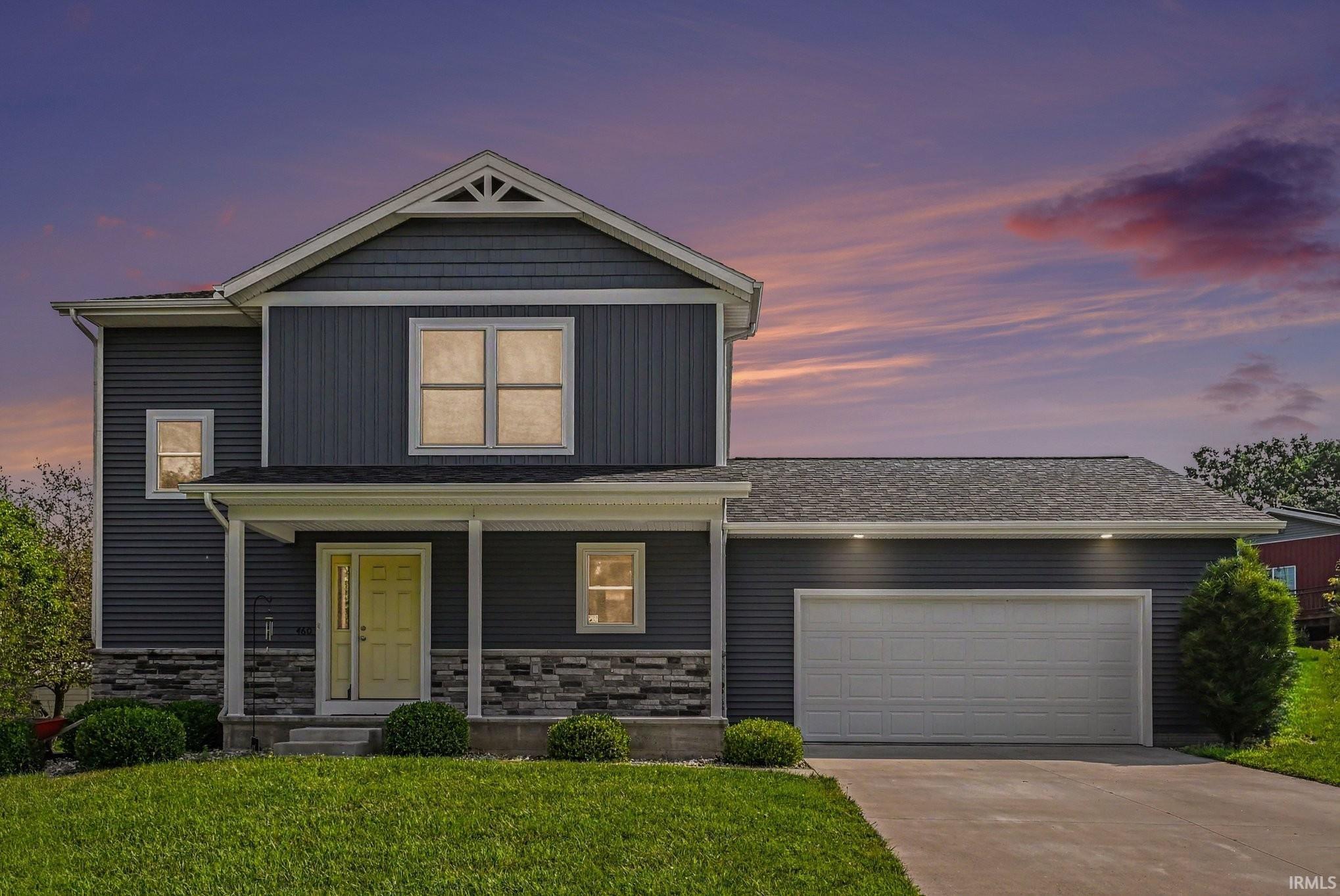 Contemporary two-story residence featuring dark siding, a covered front porch with white columns, and stone accent skirting