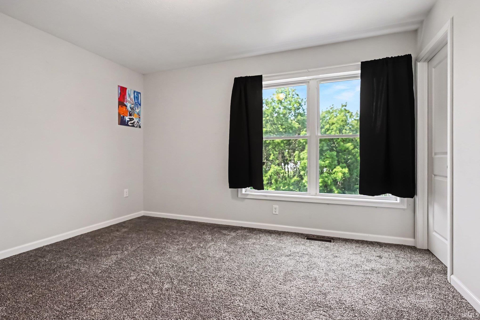 Bright room featuring a large window, plush gray carpeting, white baseboards, and a solid white door