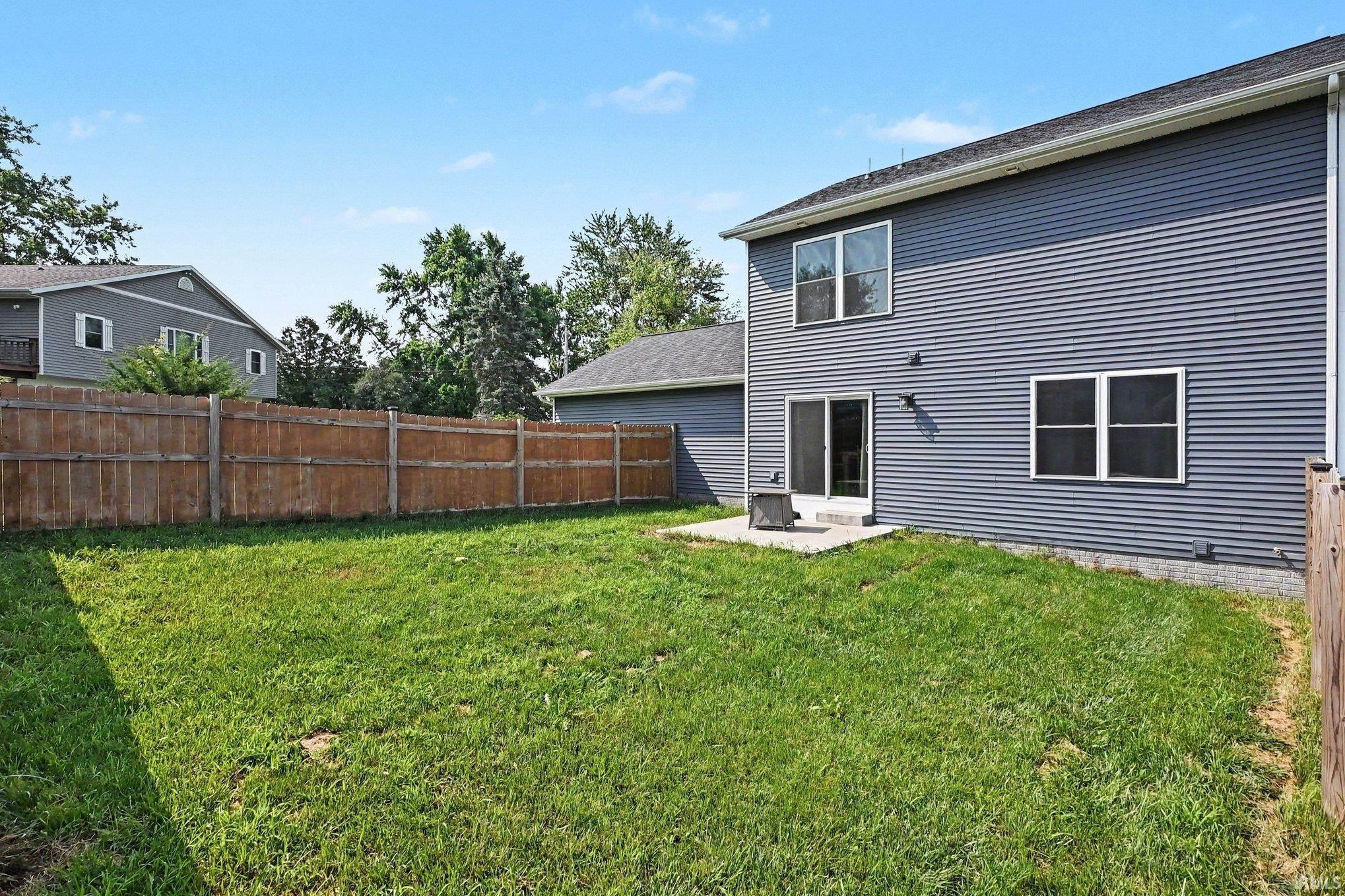Expansive green lawn framed by a wooden privacy fence, featuring a concrete patio, sliding glass doors, and two-story siding exterior