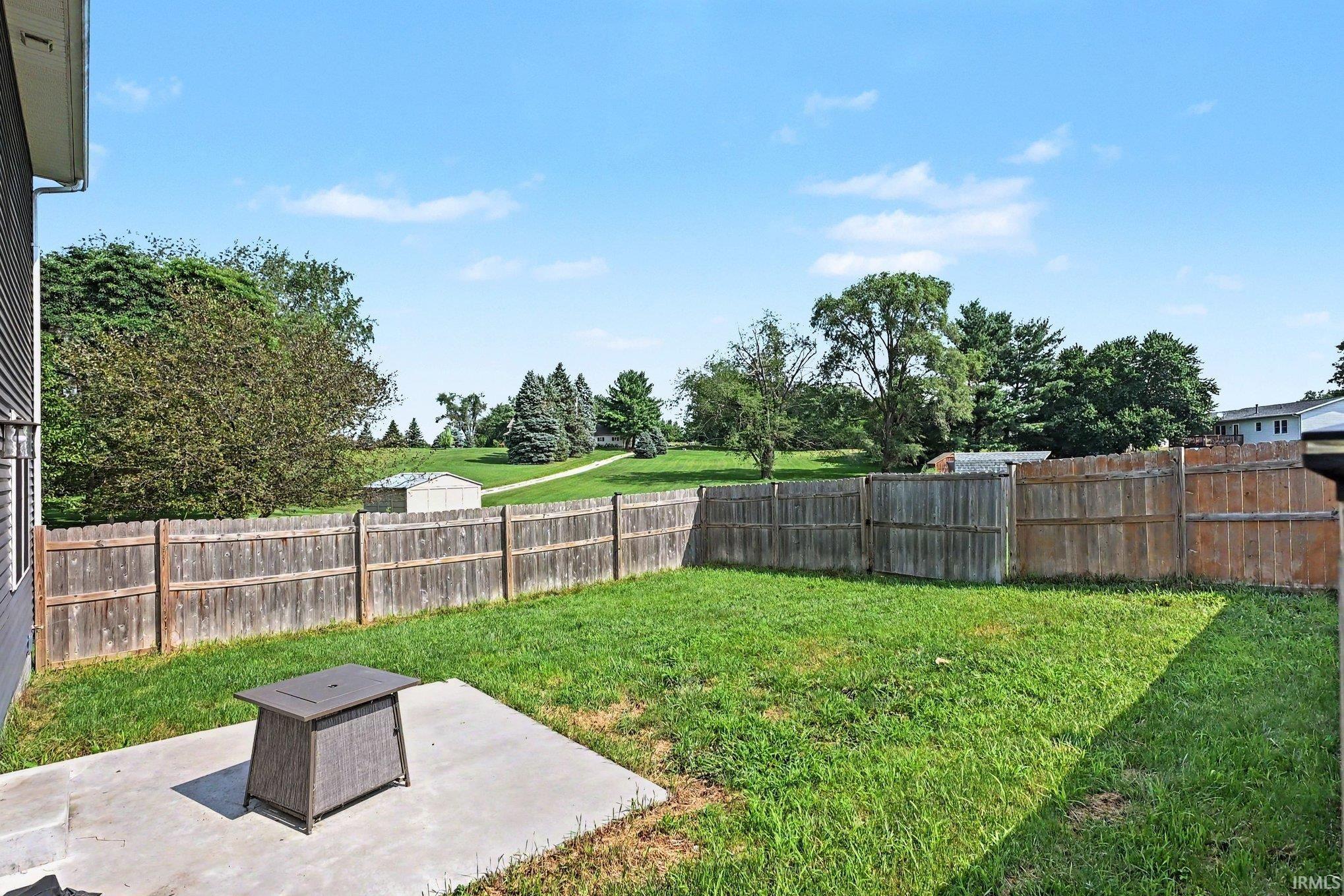 Fenced backyard featuring a concrete patio, expansive lawn, and mature perimeter landscaping
