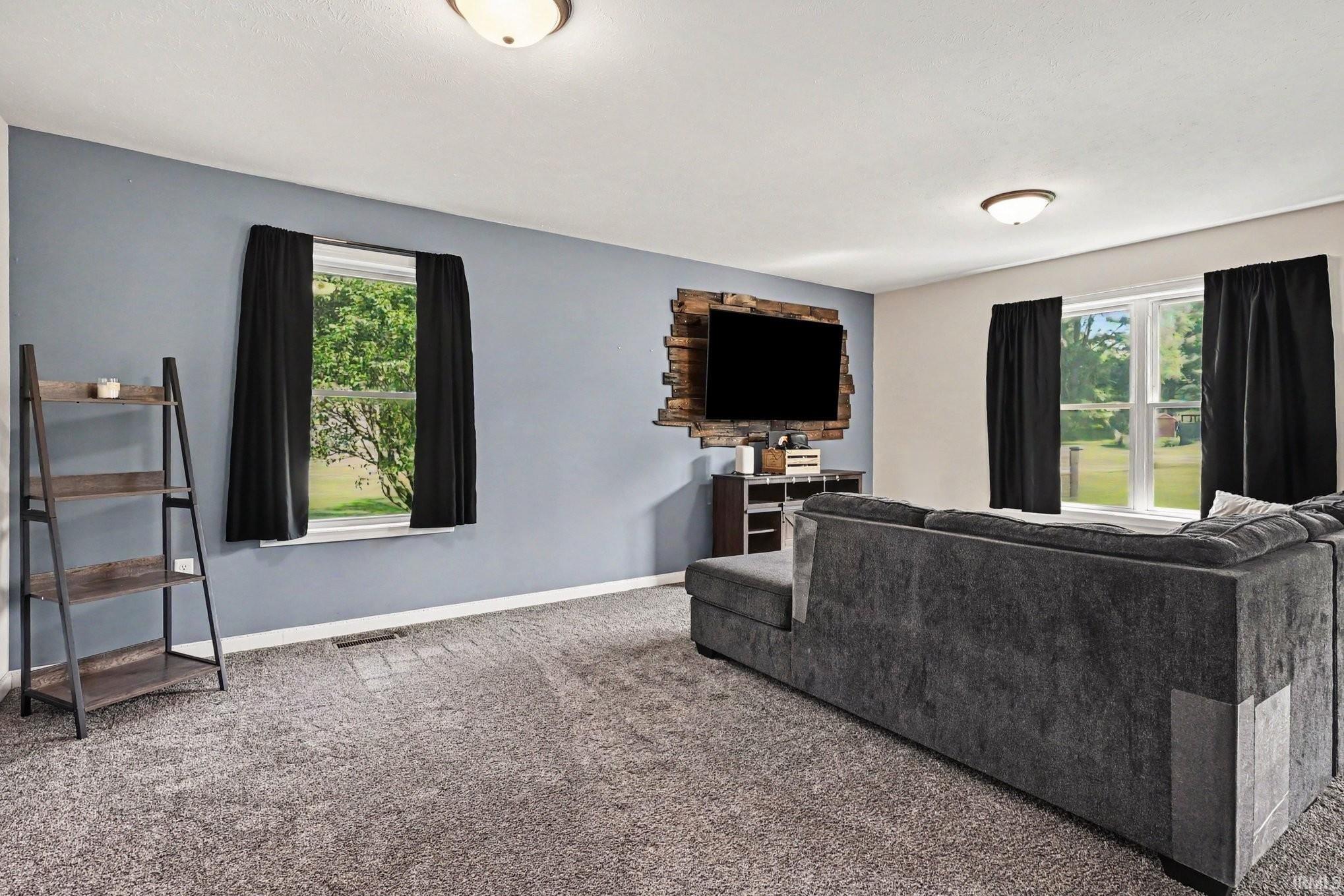 Spacious room featuring light gray carpeting, a built-in media center with a wood-paneled accent wall, and multiple windows