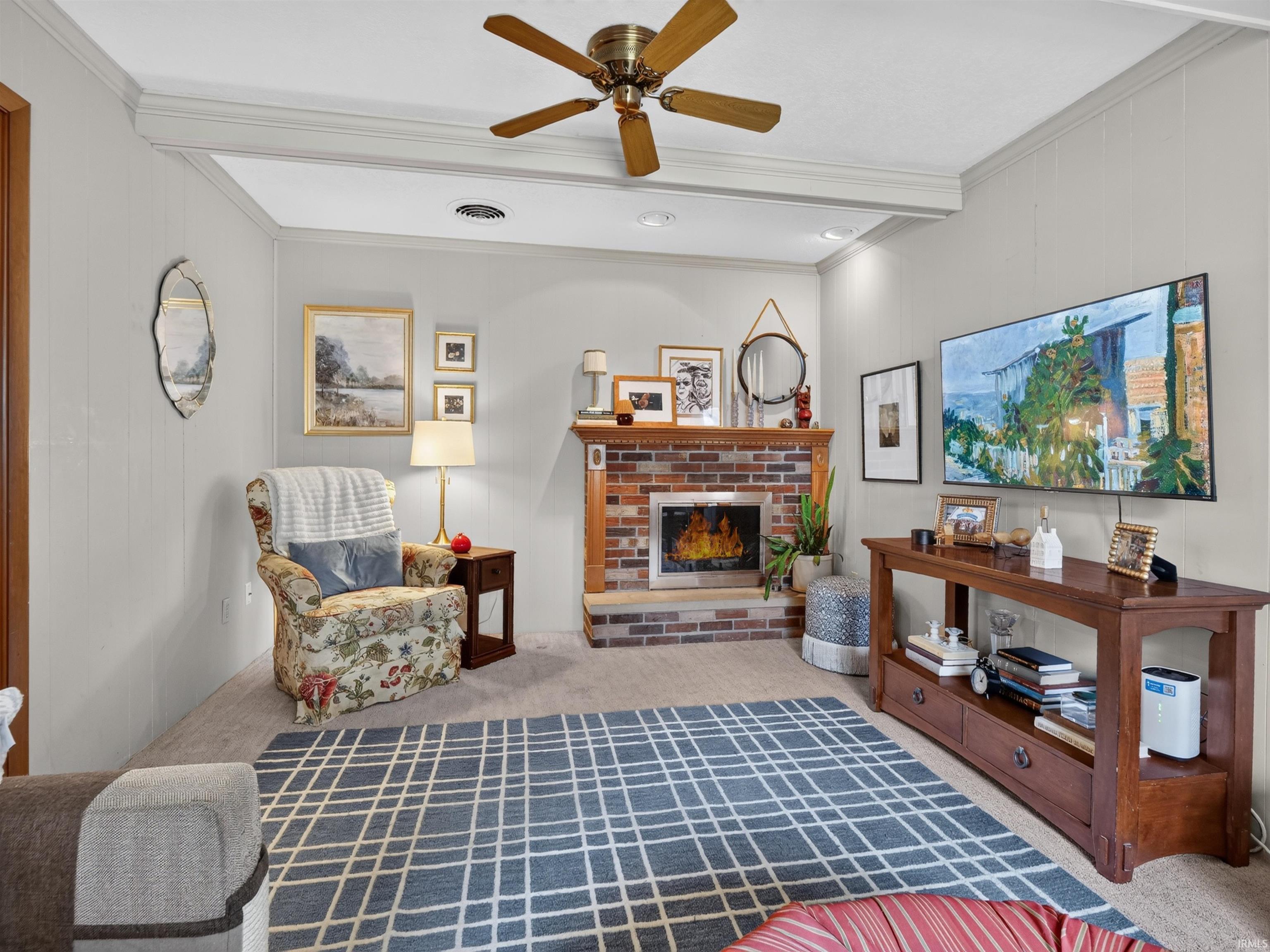 Living area featuring a gas log brick fireplace with a wood mantle, carpet flooring, a ceiling fan