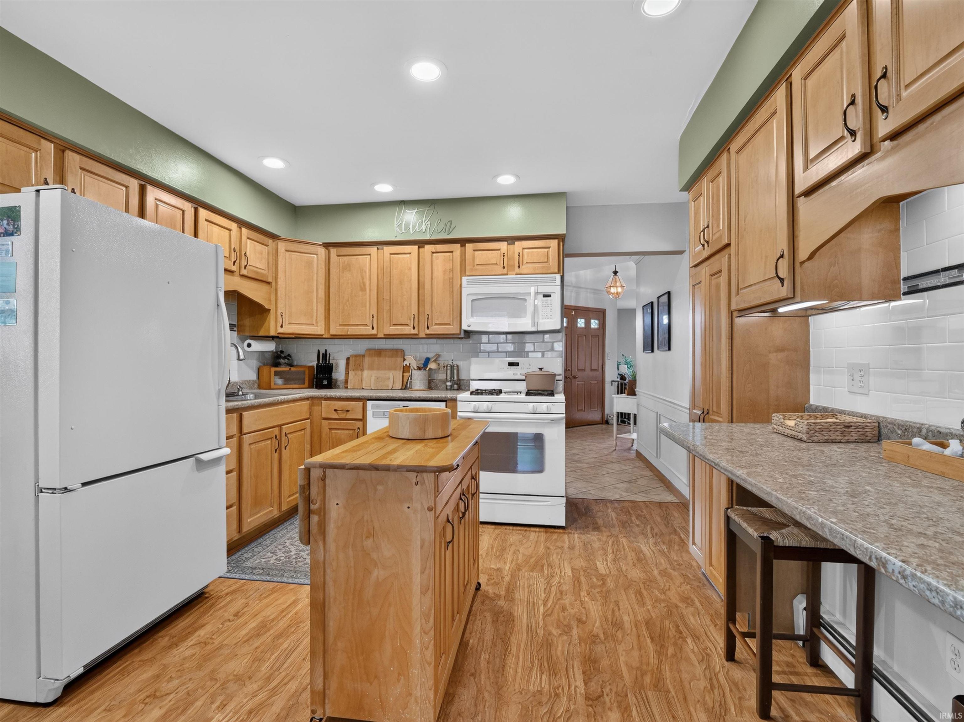 Bright kitchen featuring wood-finish flooring, light wood cabinetry, white subway tile backsplash, and a movable center island