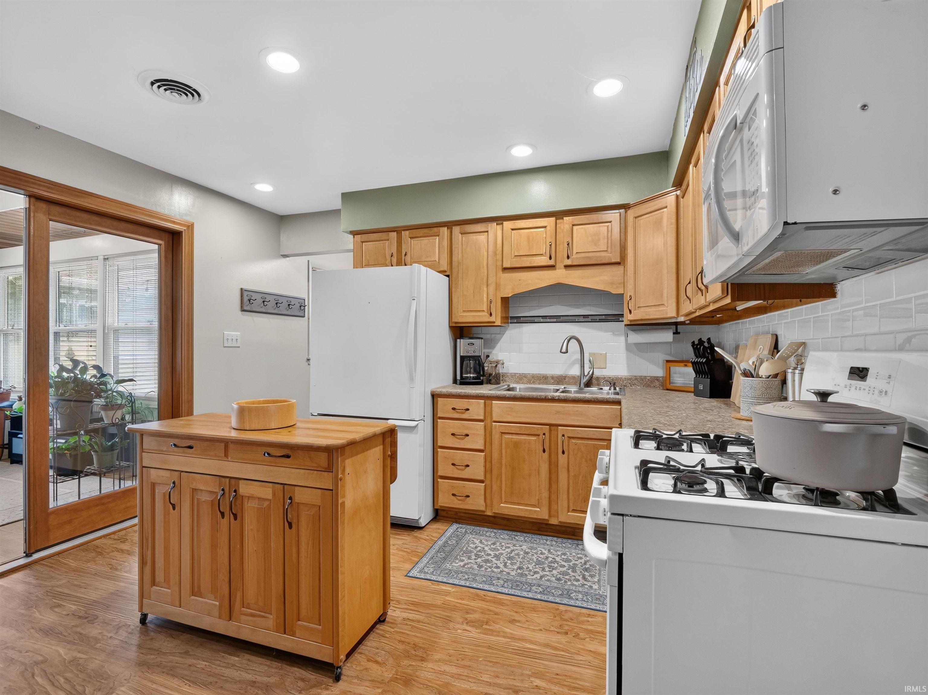 Functional kitchen featuring wood-finish flooring, light wood cabinetry, white subway tile backsplash