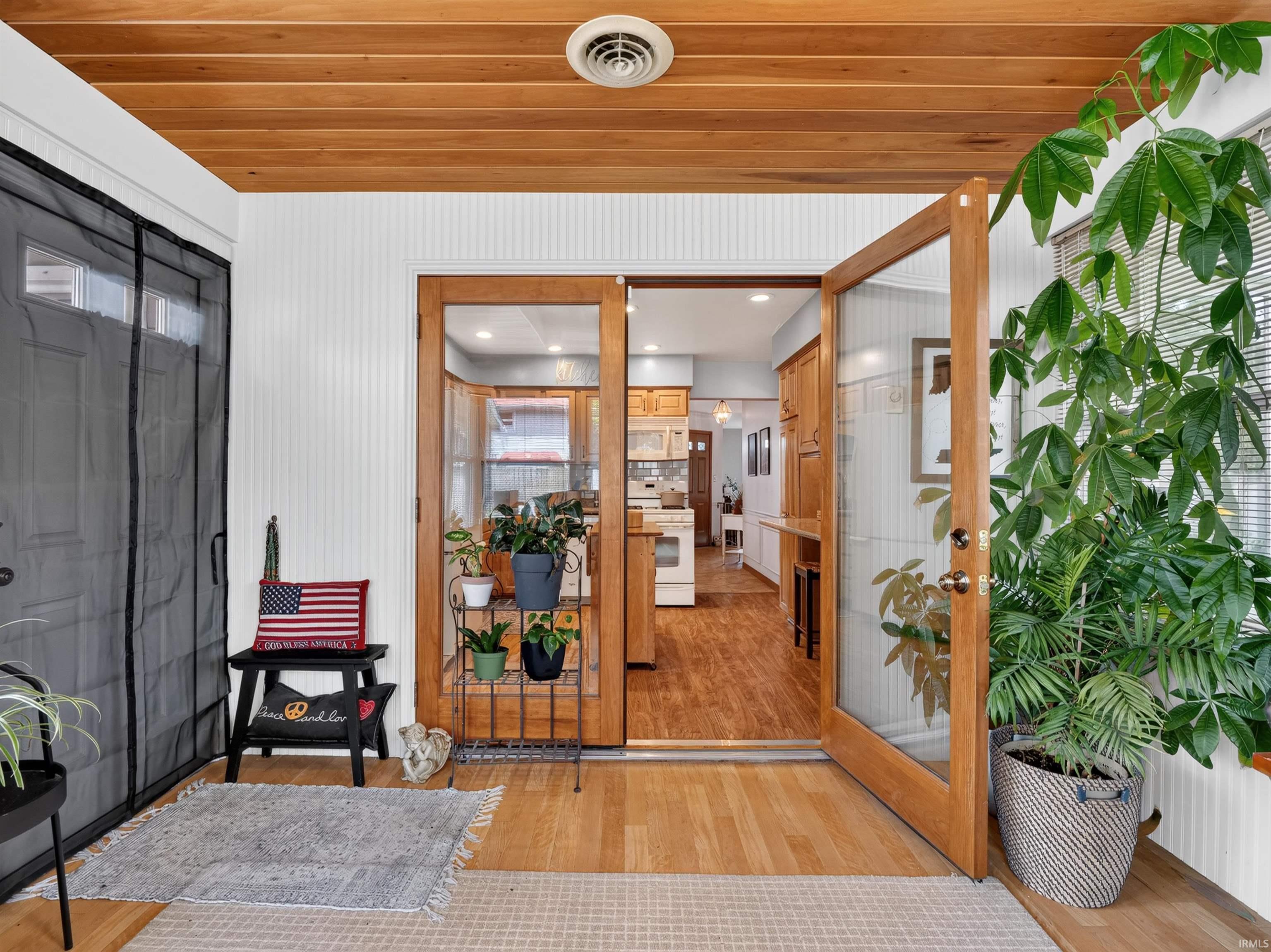 Enclosed sunroom featuring a natural wood-finish plank ceiling, wood-finish flooring, white beadboard wall paneling, and an interior wood-frame glass door