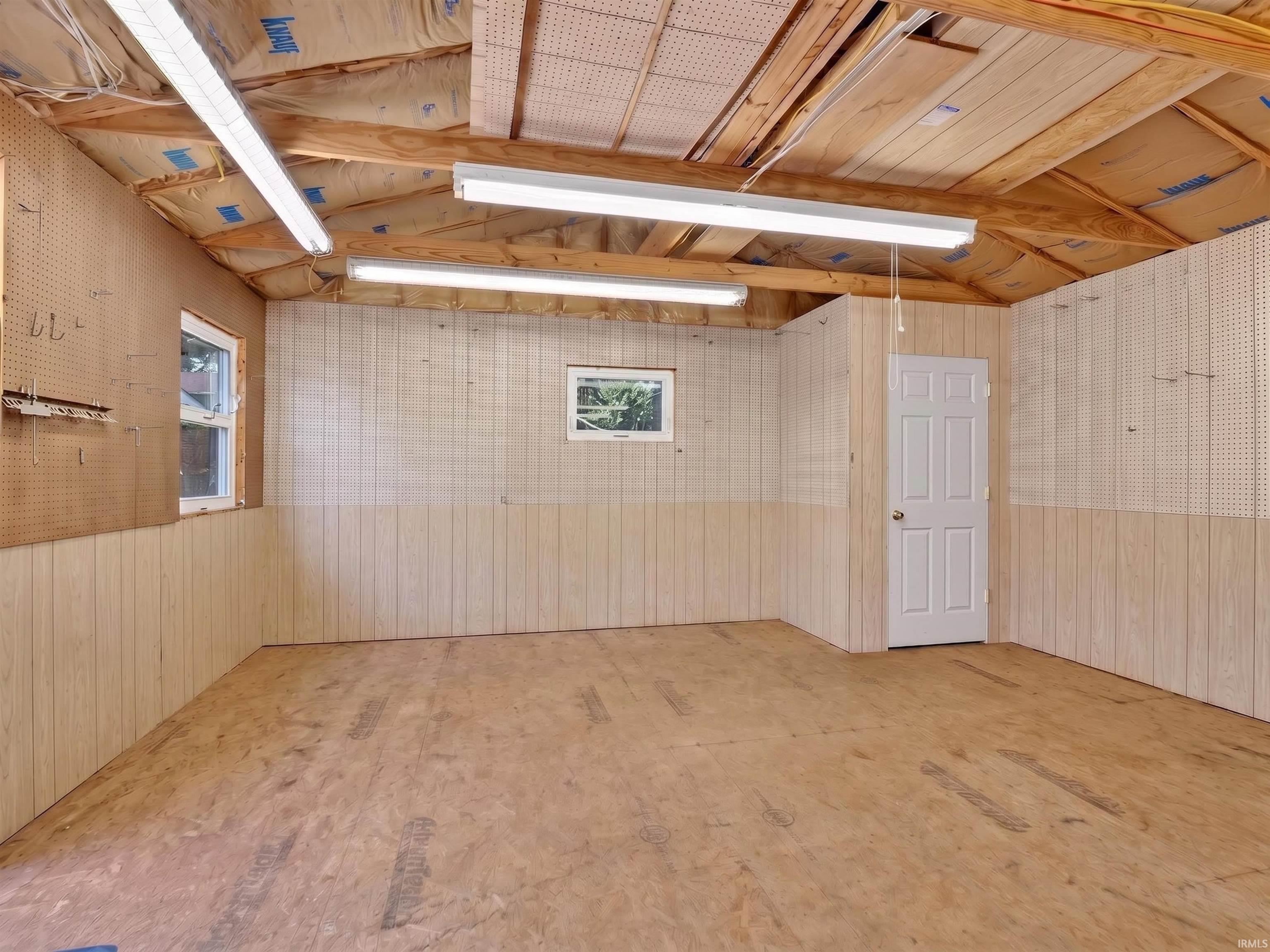 Spacious interior room featuring light-toned paneling, exposed wood ceiling beams, and plywood flooring
