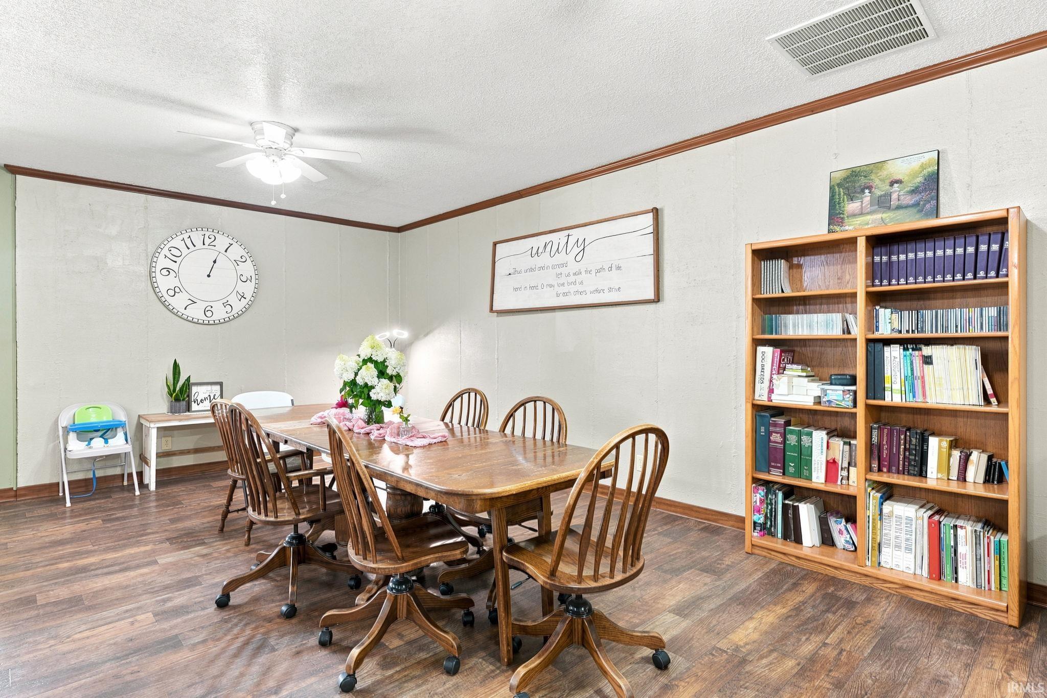 Spacious room featuring wood-finish flooring, a ceiling fan with integrated lighting, and a built-in wooden bookcase