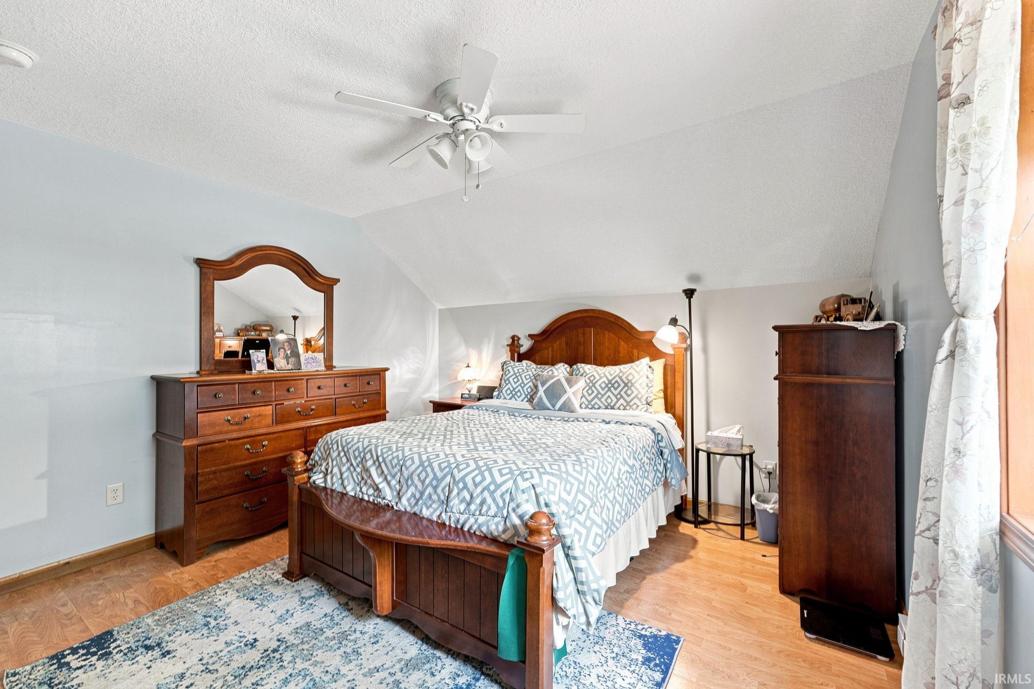 Sloped ceiling room featuring wood-finish flooring, a ceiling fan with integrated lighting, and light-toned wall finishes