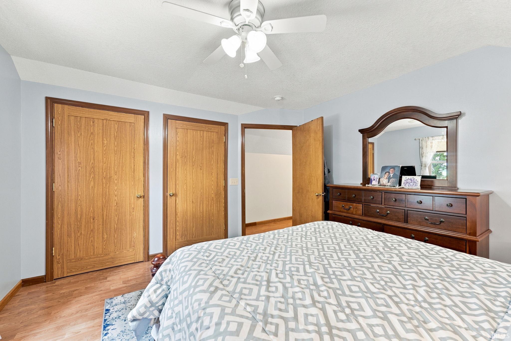 Bedroom featuring wood-finish flooring, two wood-paneled doors, and a ceiling fan with integrated lighting