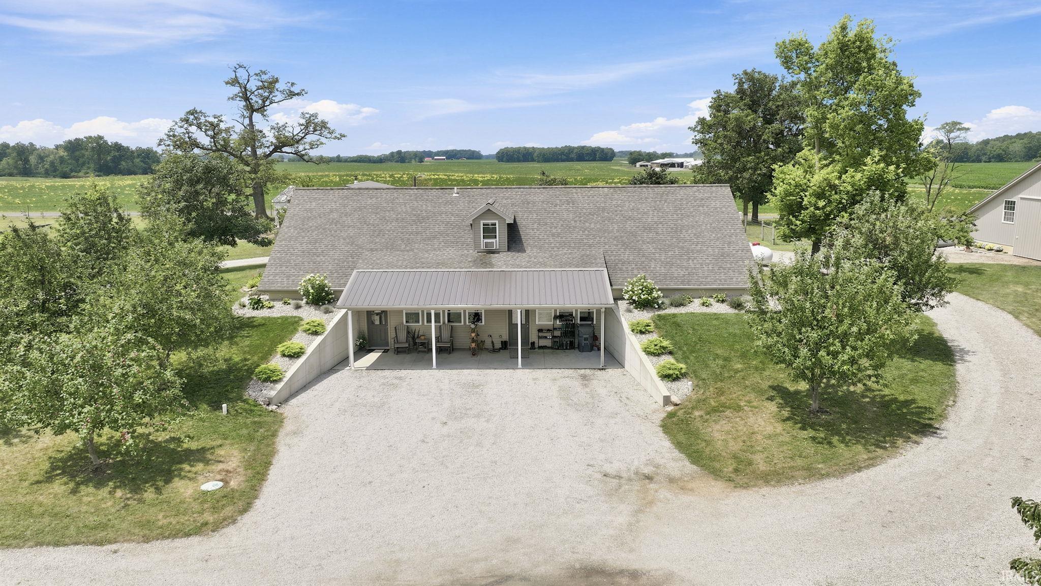 Expansive gravel driveway leading to a residence featuring a metal roofed entry, dormer, and multiple mature trees