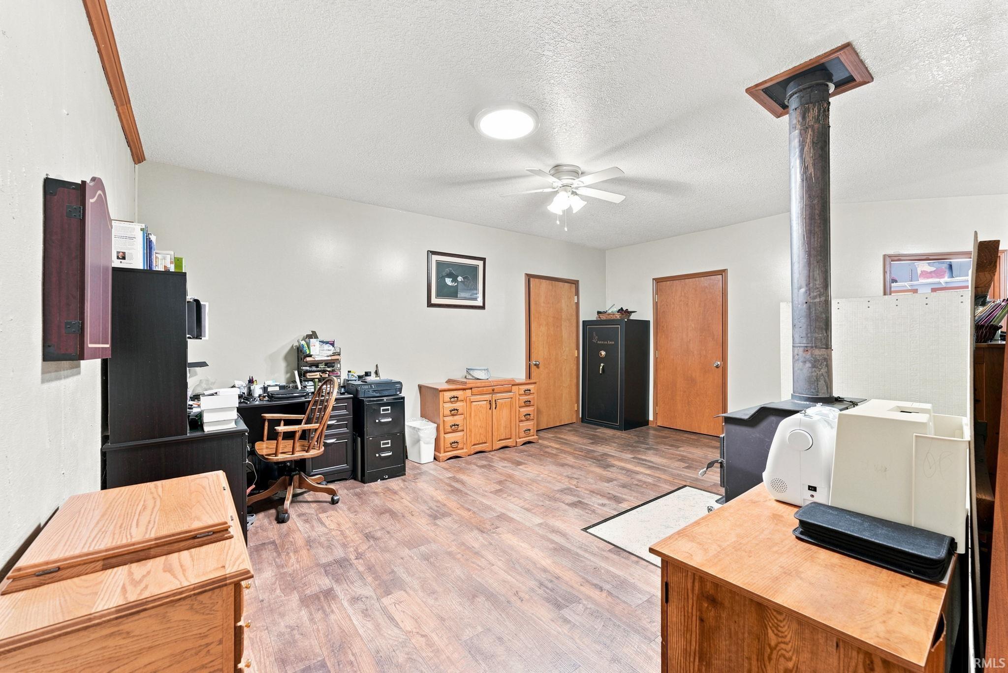 Spacious room featuring wood-finish flooring, a ceiling fan, and a built-in wood-burning stove with a metal flue